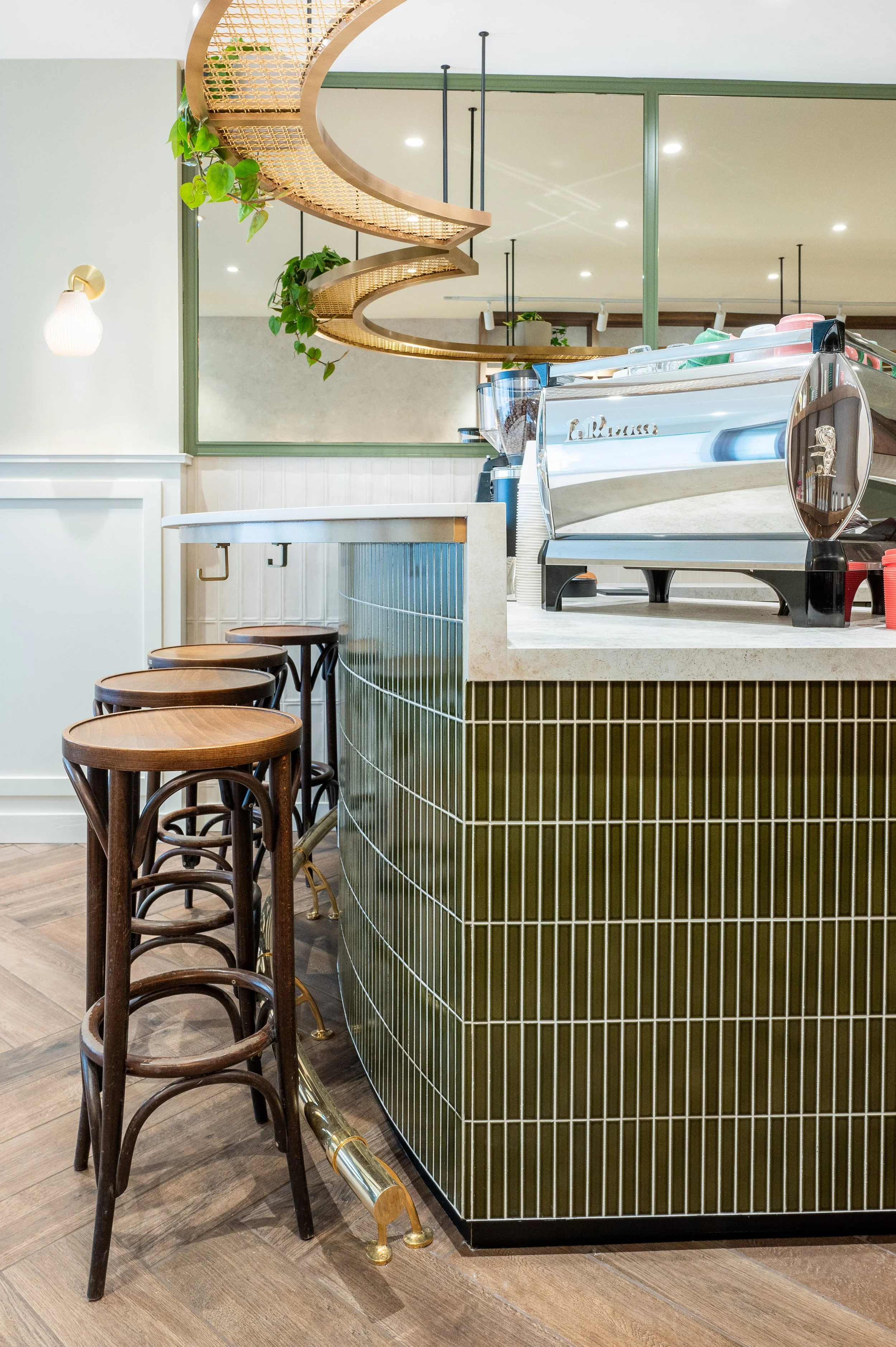 This chic café interior boasts sleek wooden shelves and curved lighting with greenery, set against a backdrop of soft green tiles. The combination of natural wood and modern design creates a warm, inviting atmosphere for coffee enthusiasts.
Discover 