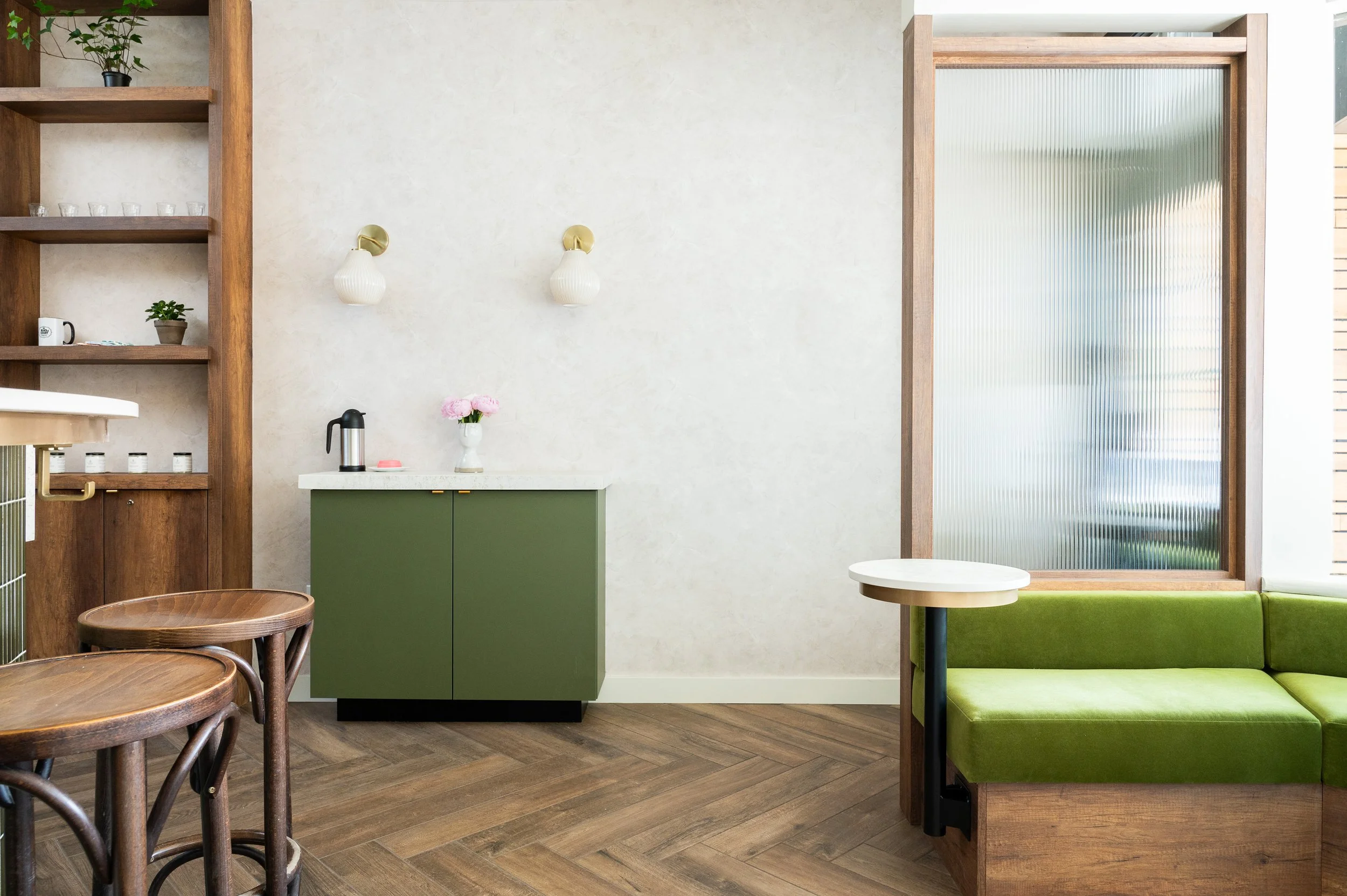 This chic café interior boasts sleek wooden shelves and curved lighting with greenery, set against a backdrop of soft green tiles. The combination of natural wood and modern design creates a warm, inviting atmosphere for coffee enthusiasts.
Discover 