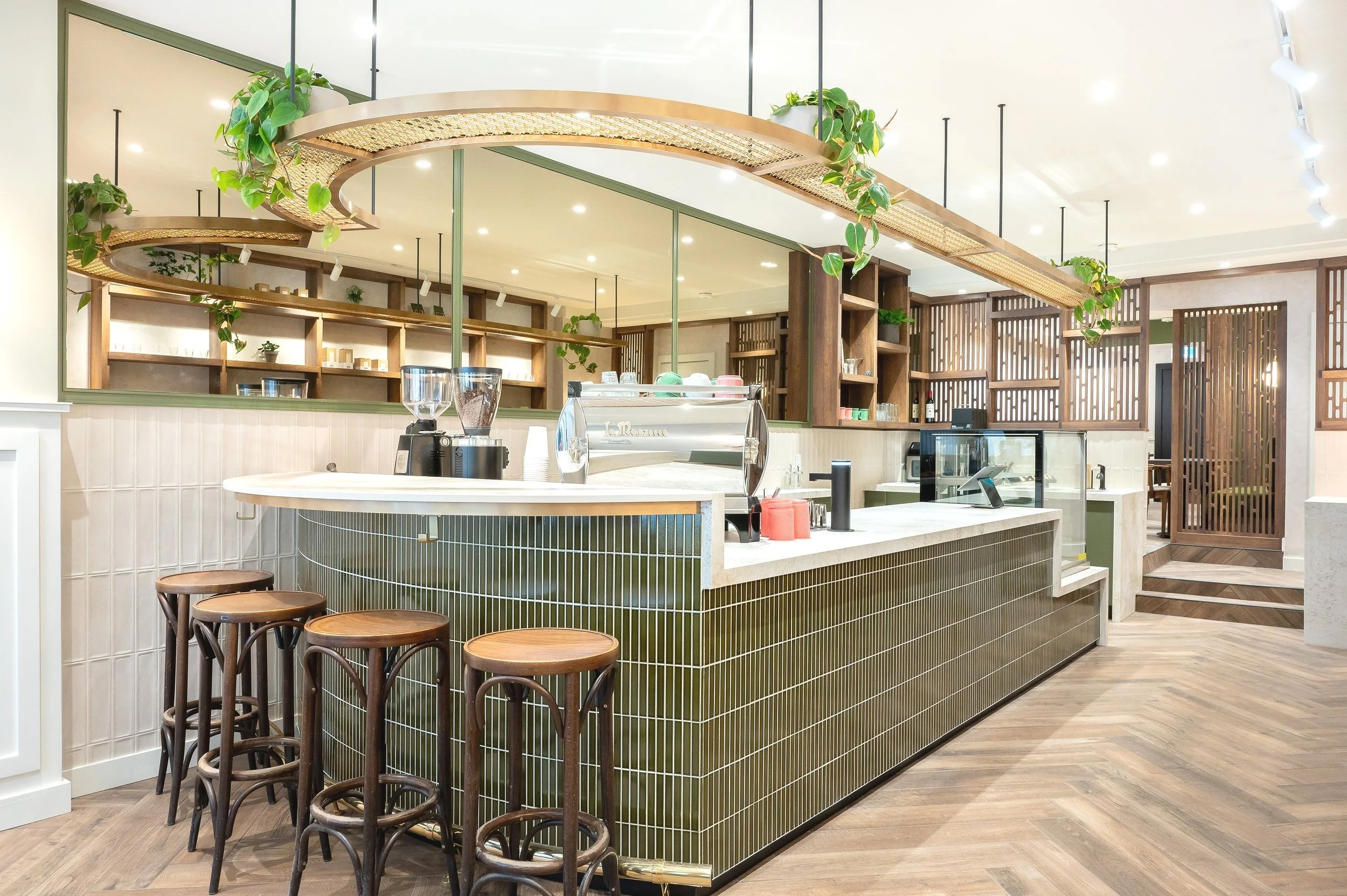 This chic café interior boasts sleek wooden shelves and curved lighting with greenery, set against a backdrop of soft green tiles. The combination of natural wood and modern design creates a warm, inviting atmosphere for coffee enthusiasts.
Discover 