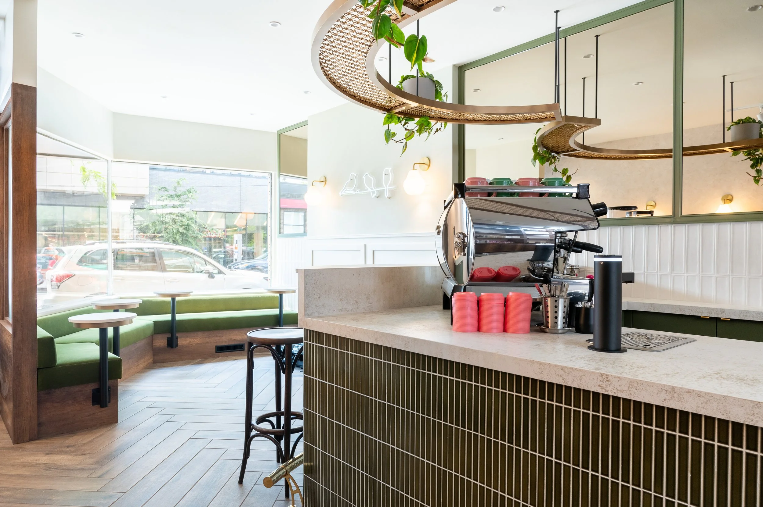 This chic café interior boasts sleek wooden shelves and curved lighting with greenery, set against a backdrop of soft green tiles. The combination of natural wood and modern design creates a warm, inviting atmosphere for coffee enthusiasts.
Discover 