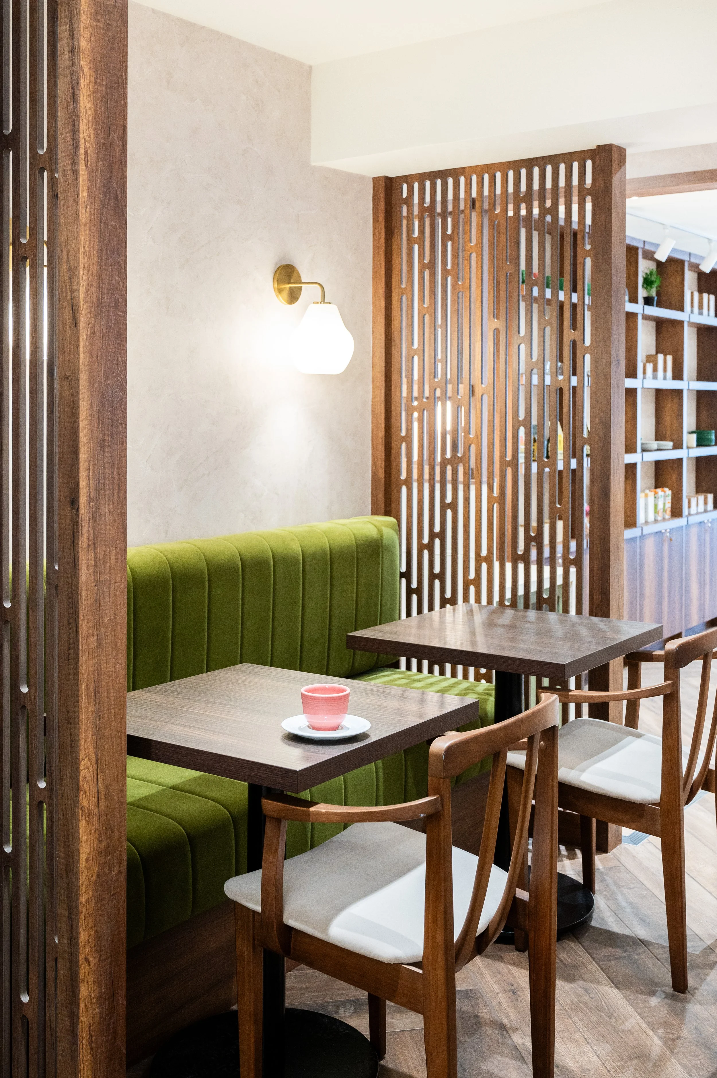 This chic café interior boasts sleek wooden shelves and curved lighting with greenery, set against a backdrop of soft green tiles. The combination of natural wood and modern design creates a warm, inviting atmosphere for coffee enthusiasts.
Discover 