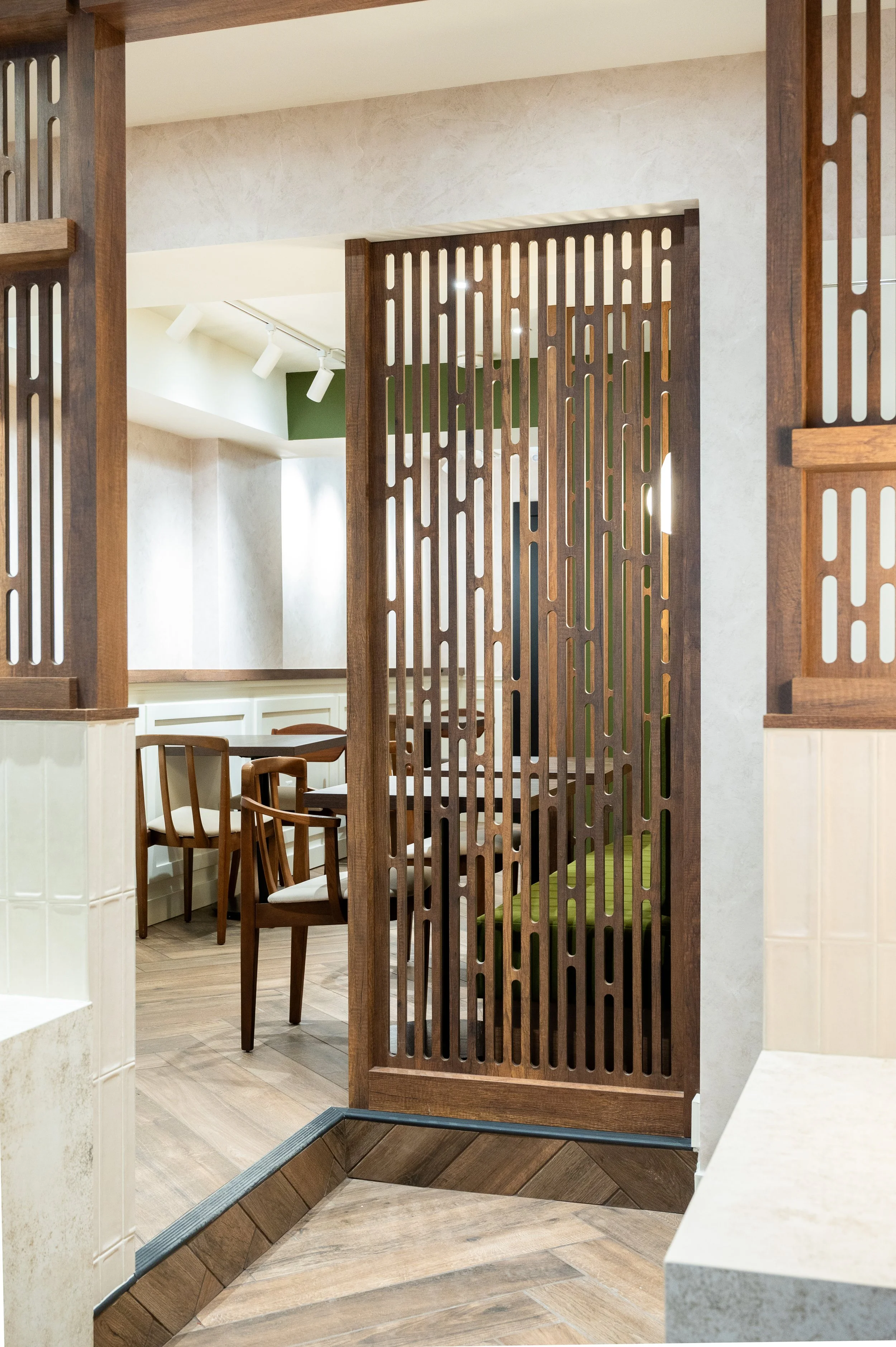 This chic café interior boasts sleek wooden shelves and curved lighting with greenery, set against a backdrop of soft green tiles. The combination of natural wood and modern design creates a warm, inviting atmosphere for coffee enthusiasts.
Discover 