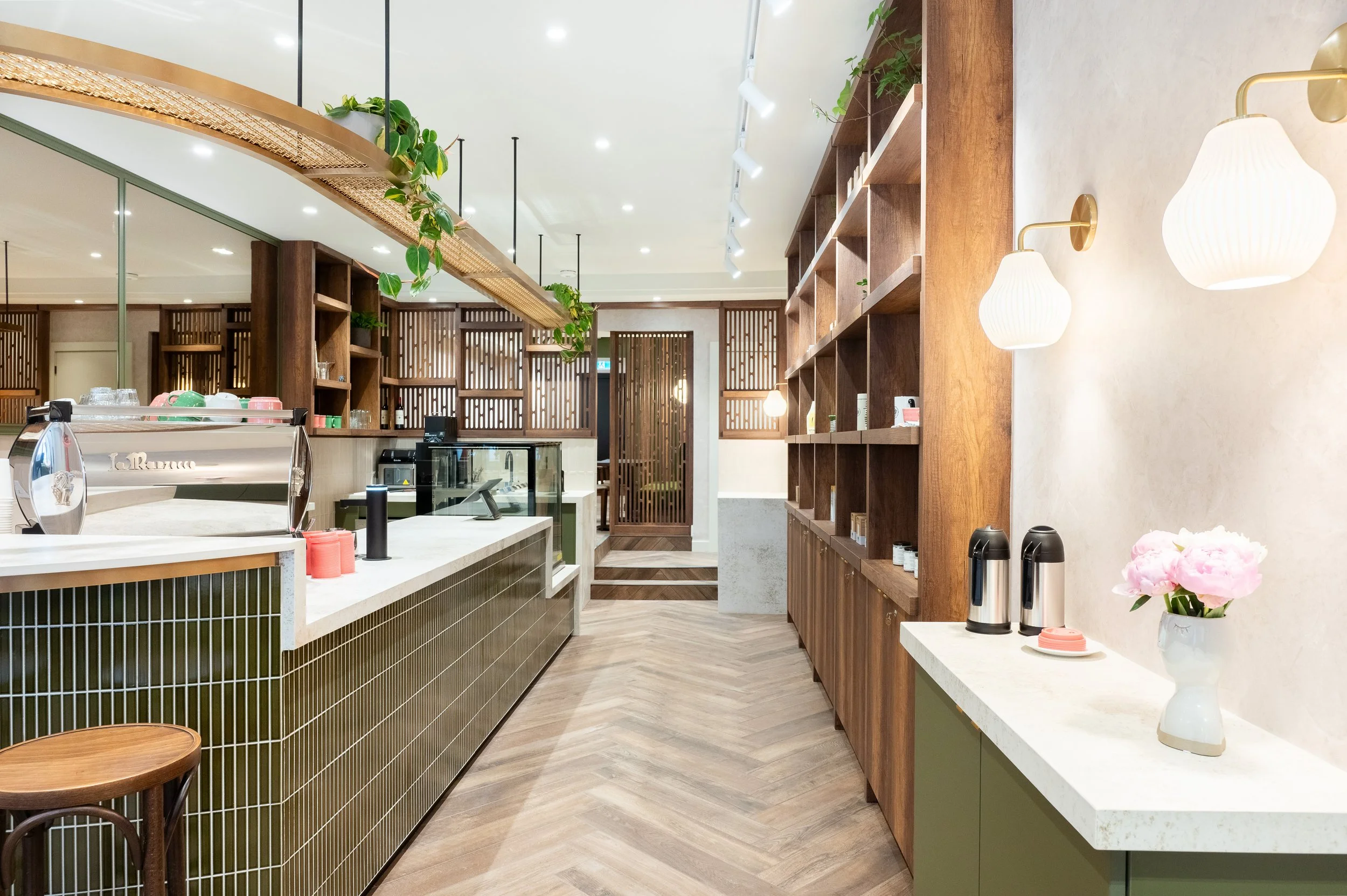 This chic café interior boasts sleek wooden shelves and curved lighting with greenery, set against a backdrop of soft green tiles. The combination of natural wood and modern design creates a warm, inviting atmosphere for coffee enthusiasts.
Discover 