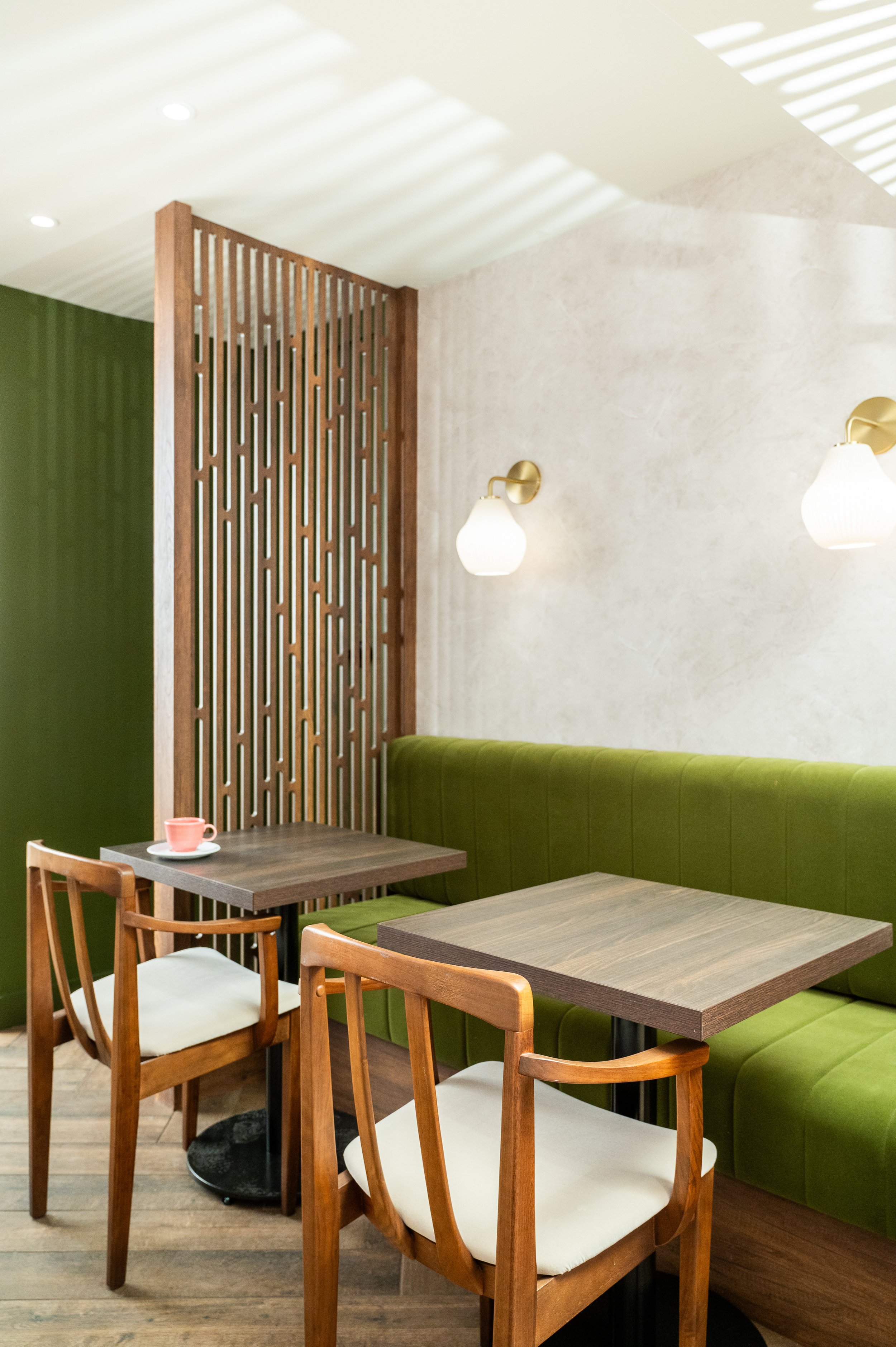 This chic café interior boasts sleek wooden shelves and curved lighting with greenery, set against a backdrop of soft green tiles. The combination of natural wood and modern design creates a warm, inviting atmosphere for coffee enthusiasts.
Discover 