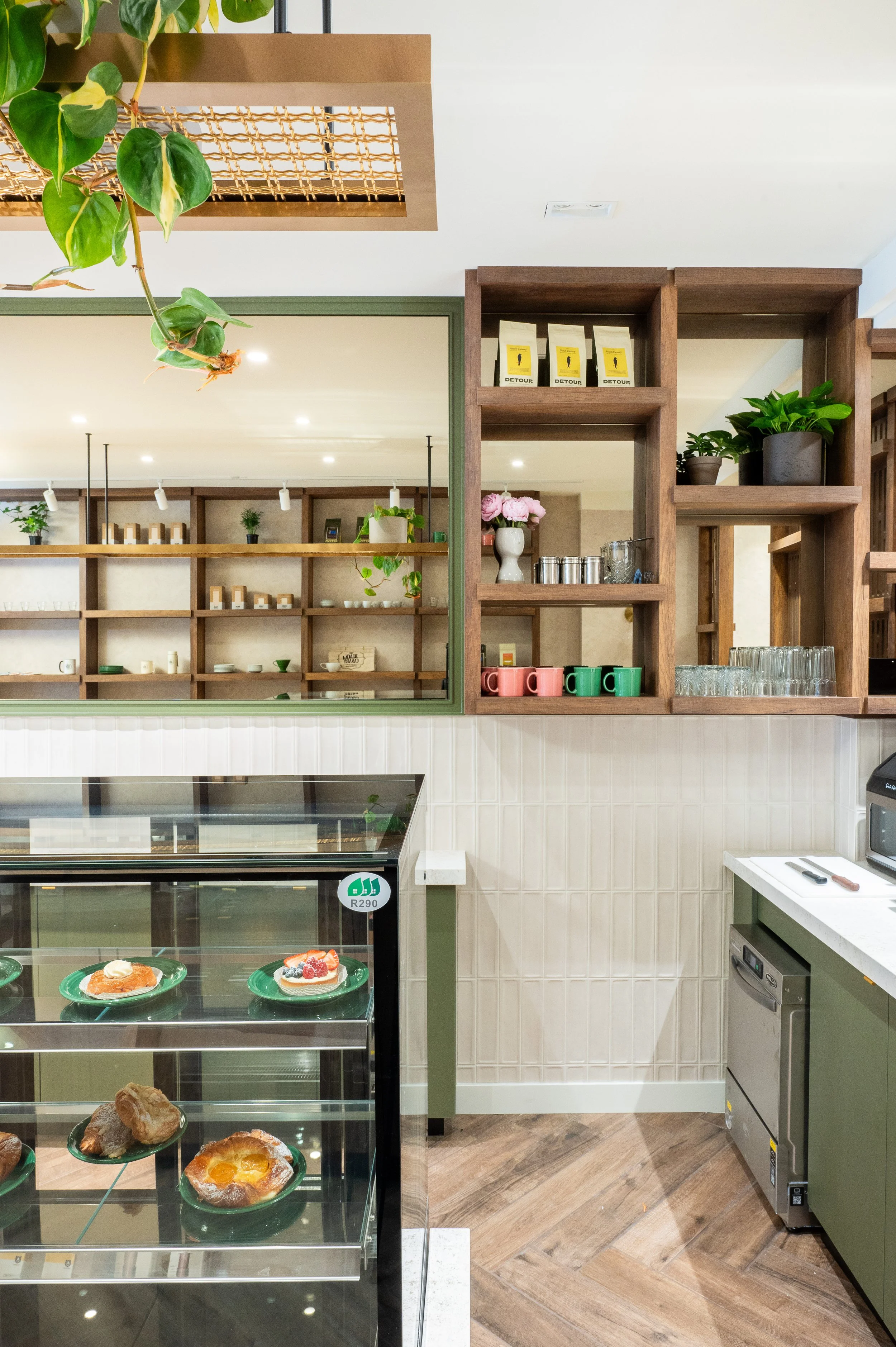 This chic café interior boasts sleek wooden shelves and curved lighting with greenery, set against a backdrop of soft green tiles. The combination of natural wood and modern design creates a warm, inviting atmosphere for coffee enthusiasts.
Discover 