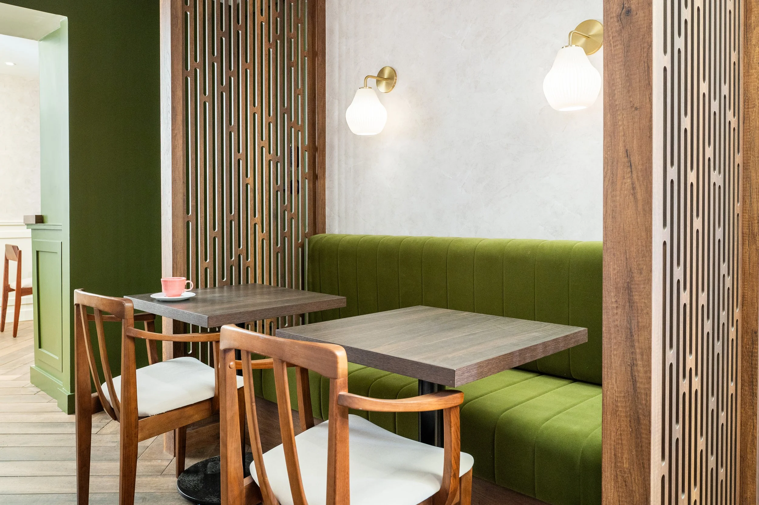This chic café interior boasts sleek wooden shelves and curved lighting with greenery, set against a backdrop of soft green tiles. The combination of natural wood and modern design creates a warm, inviting atmosphere for coffee enthusiasts.
Discover 