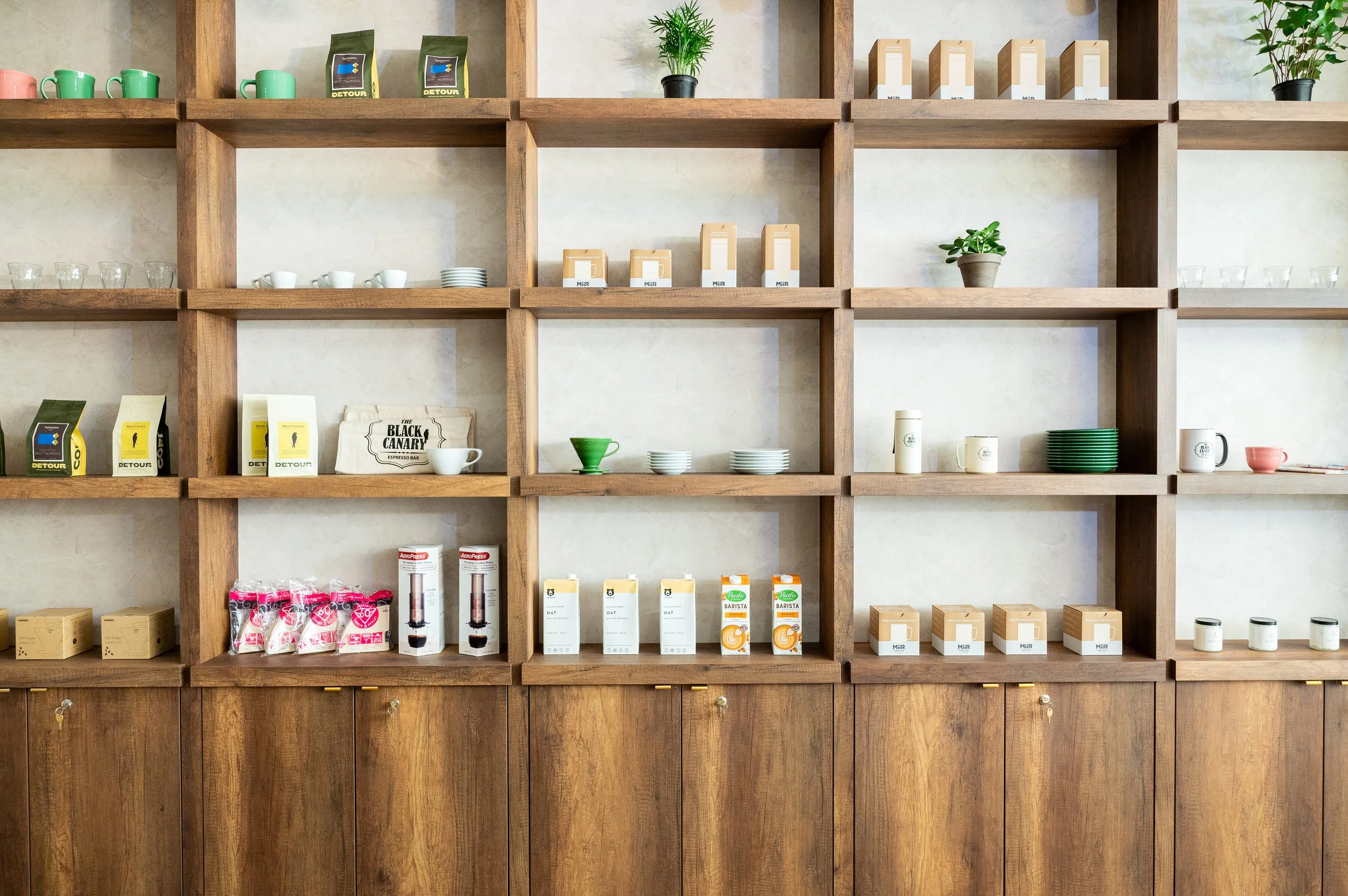 This chic café interior boasts sleek wooden shelves and curved lighting with greenery, set against a backdrop of soft green tiles. The combination of natural wood and modern design creates a warm, inviting atmosphere for coffee enthusiasts.
Discover 