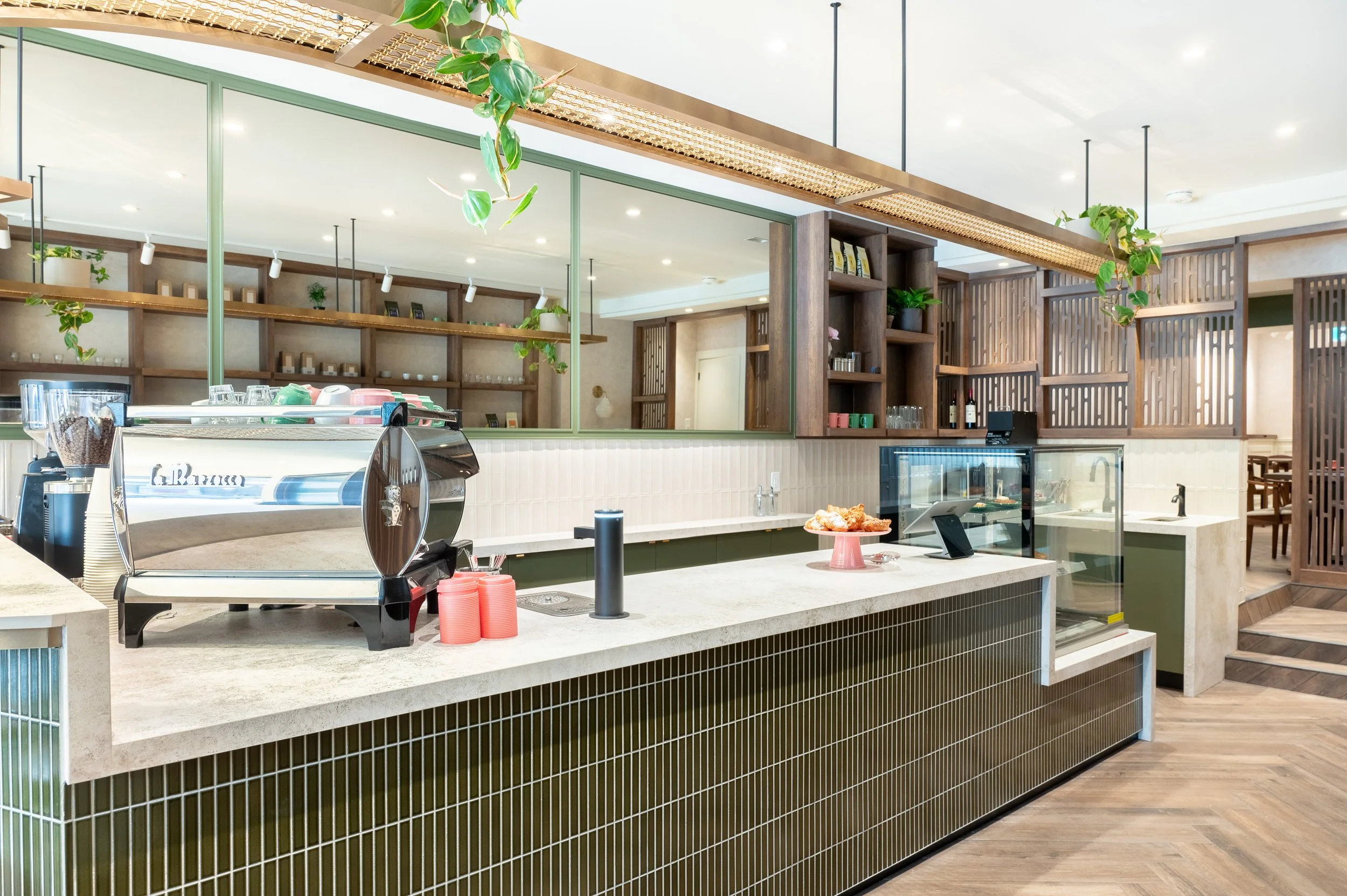 This chic café interior boasts sleek wooden shelves and curved lighting with greenery, set against a backdrop of soft green tiles. The combination of natural wood and modern design creates a warm, inviting atmosphere for coffee enthusiasts.
Discover 