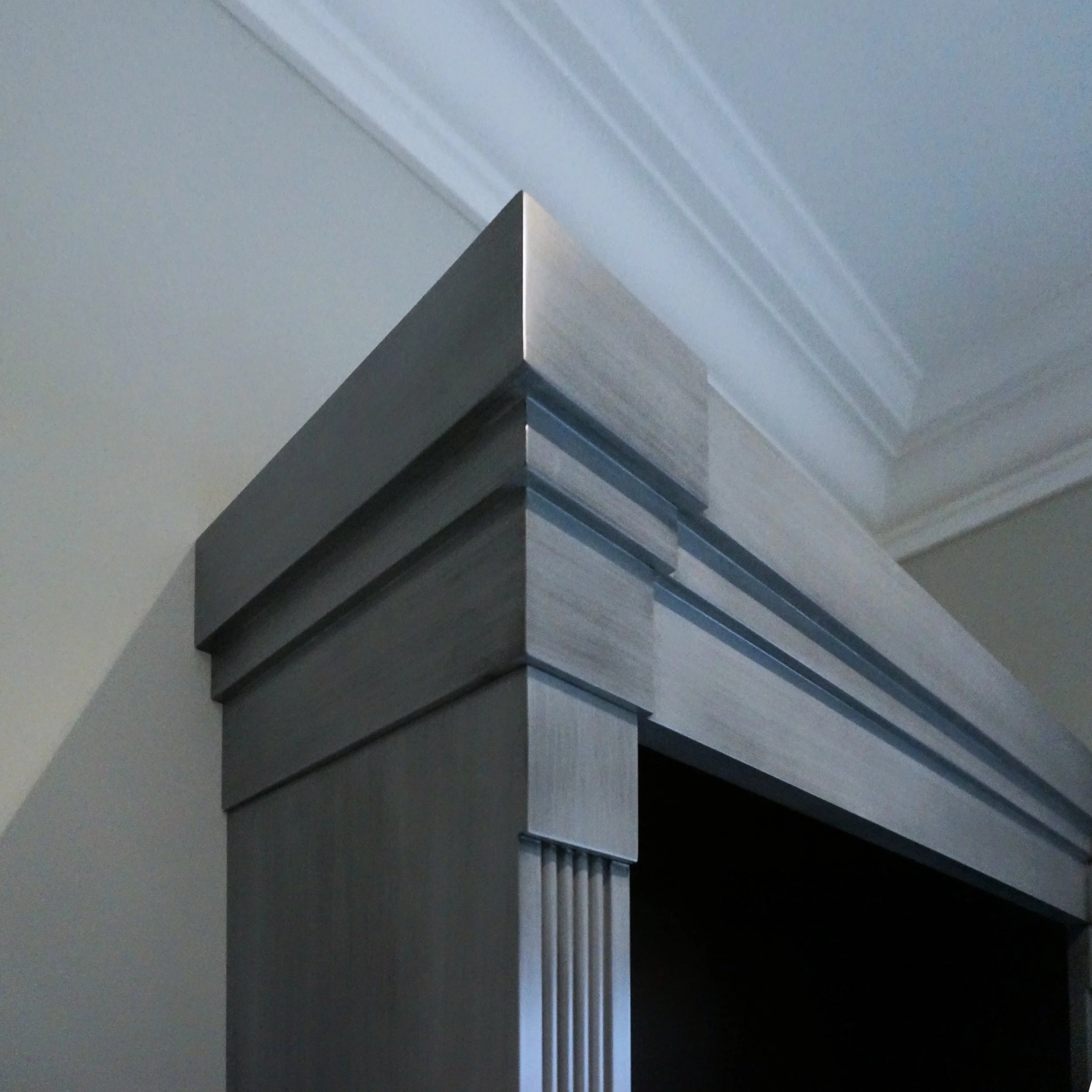 A close-up of a staircase bannister with a modern design, featuring diagonal black and gray panels and a light-colored railing with vertical white balusters.