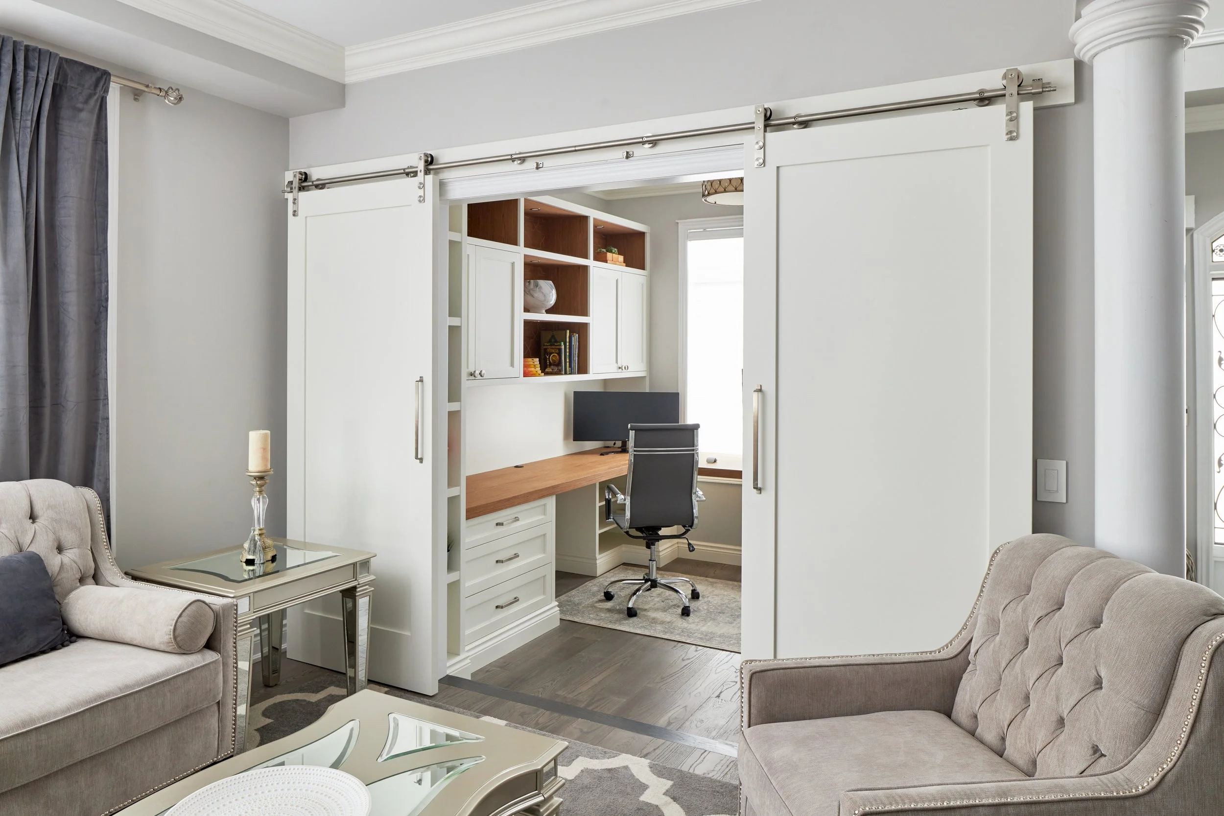 Living room with beige sofas, glass coffee table, gray curtains, and a home office area separated by sliding barn doors with a desk and black office chair.