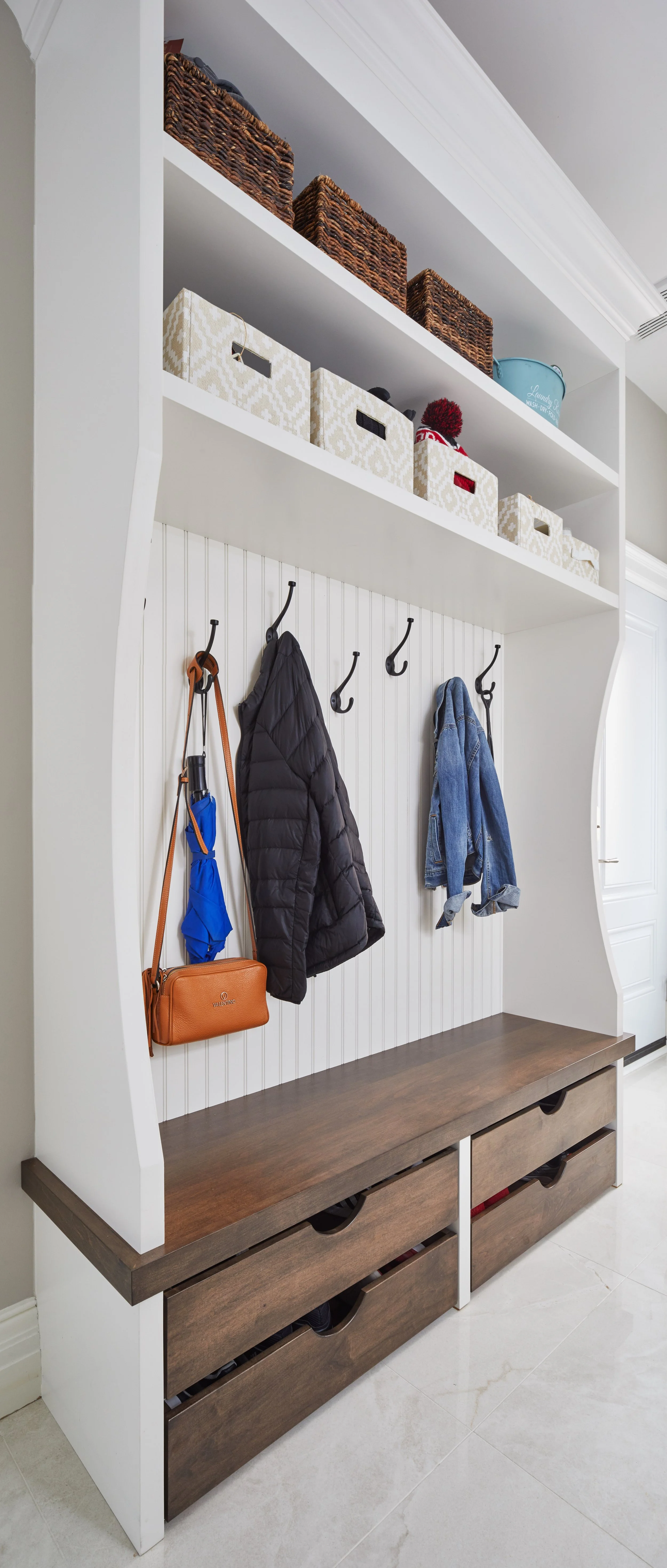 Entryway storage with hooks and shelves holding coats, bags, and storage baskets.