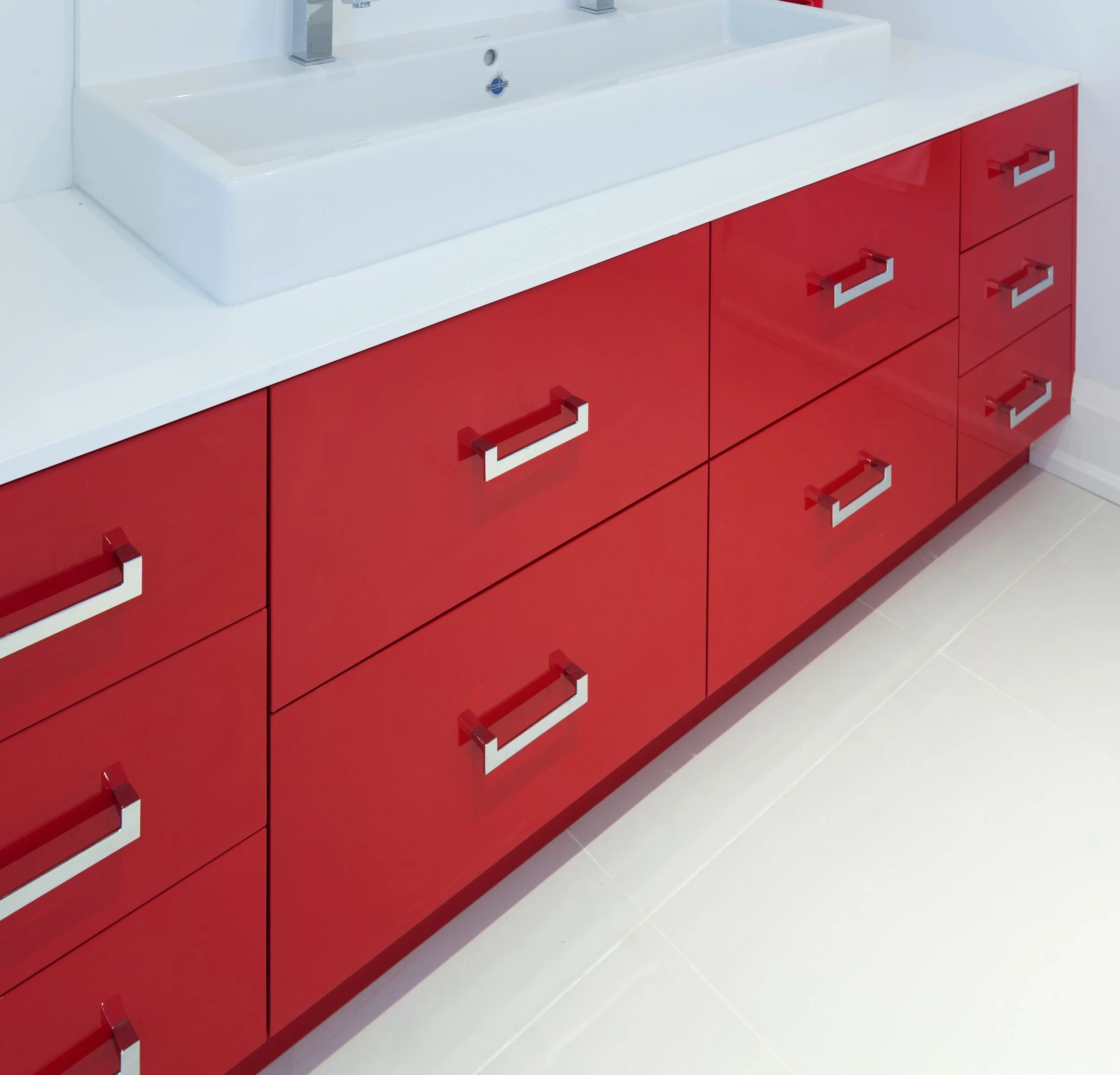 Red cabinet with multiple drawers and chrome handles, white countertop, and a white sink with a shiny, modern faucet.