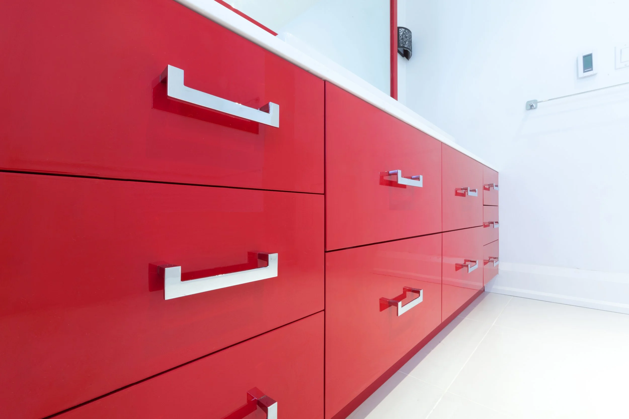 Close-up of a red cabinet with shiny silver handles against a white wall in a modern, minimalist room.