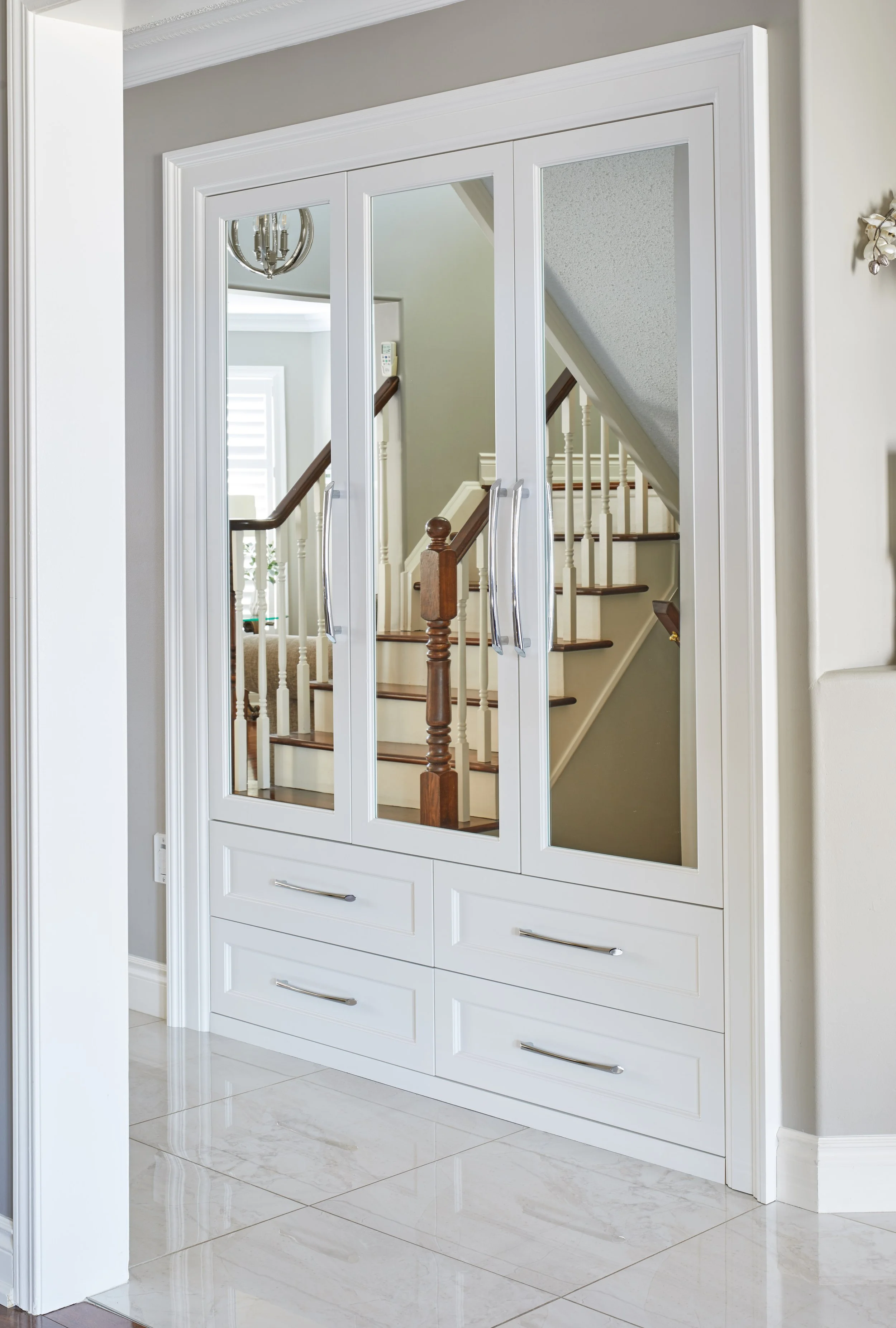 White-glass front cabinet with drawers underneath, situated in entryway with white marble floor.