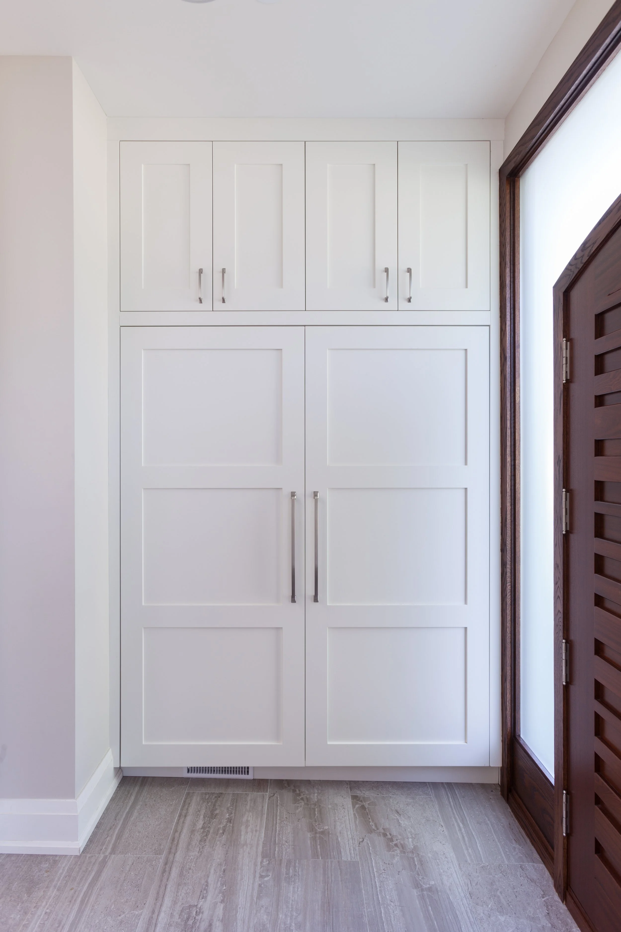 Interior view of a kitchen corner with white built-in cabinets, a wooden door on the right, and tiled flooring.