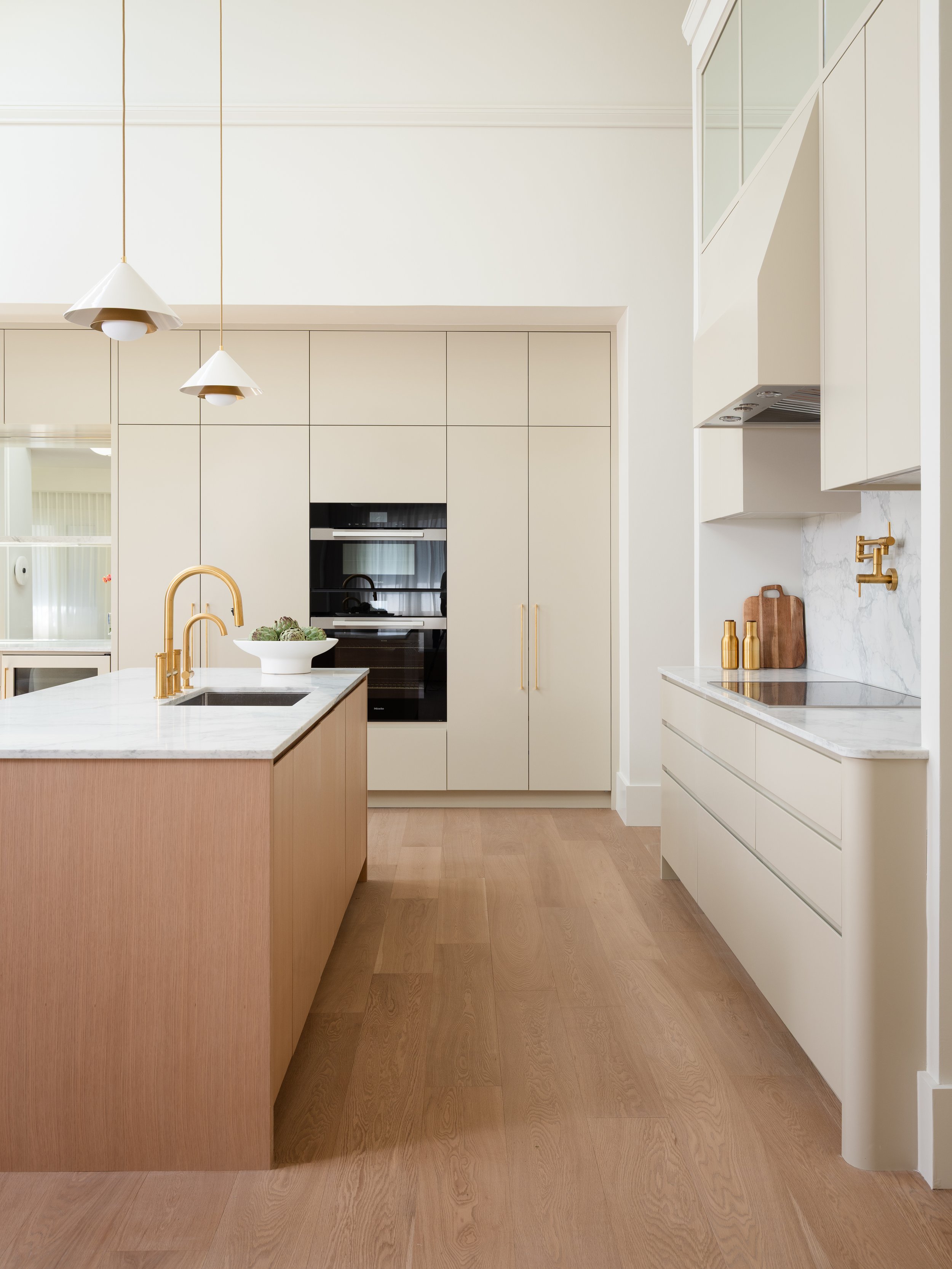 Modern kitchen with white cabinets, a kitchen island with a white marble countertop, gold fixtures, pendant lights, and a wood floor.