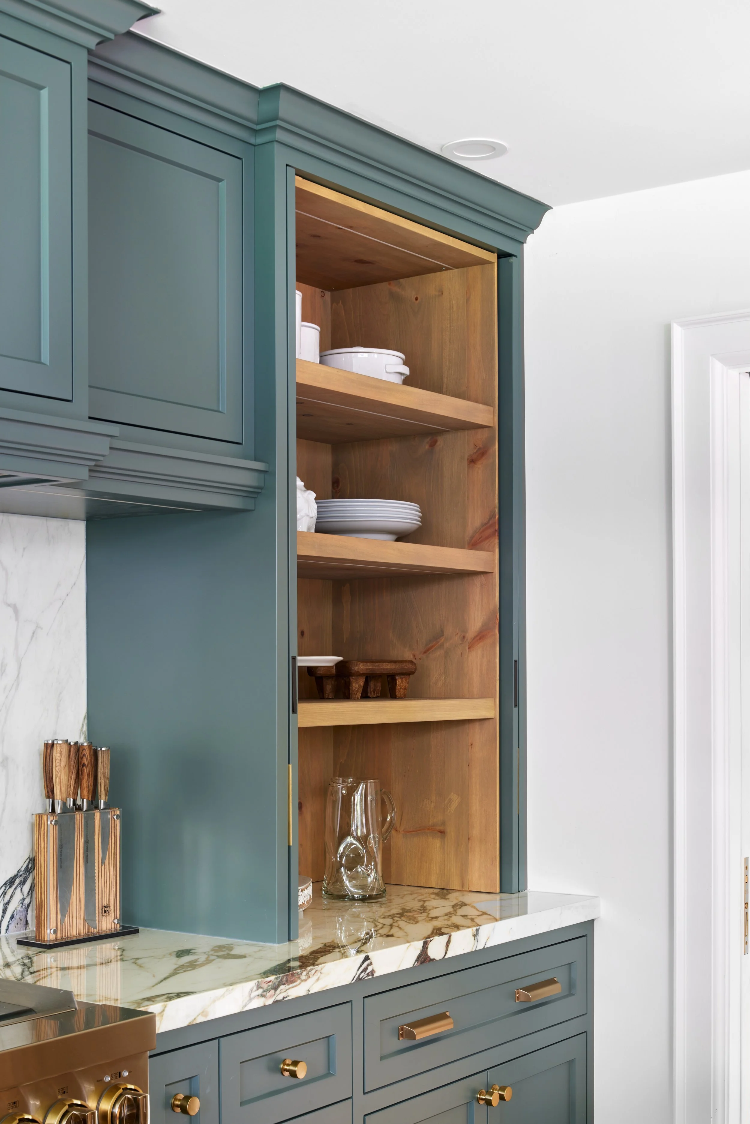 High-end custom modern kitchen in Mississauga, Oakville, and Toronto, Ontario. Features trends color for 2024, luxurious gold hardware, a marble countertop, an elegant kitchen sink, and custom shelving with a pocket door. Serving millwork and cabinet