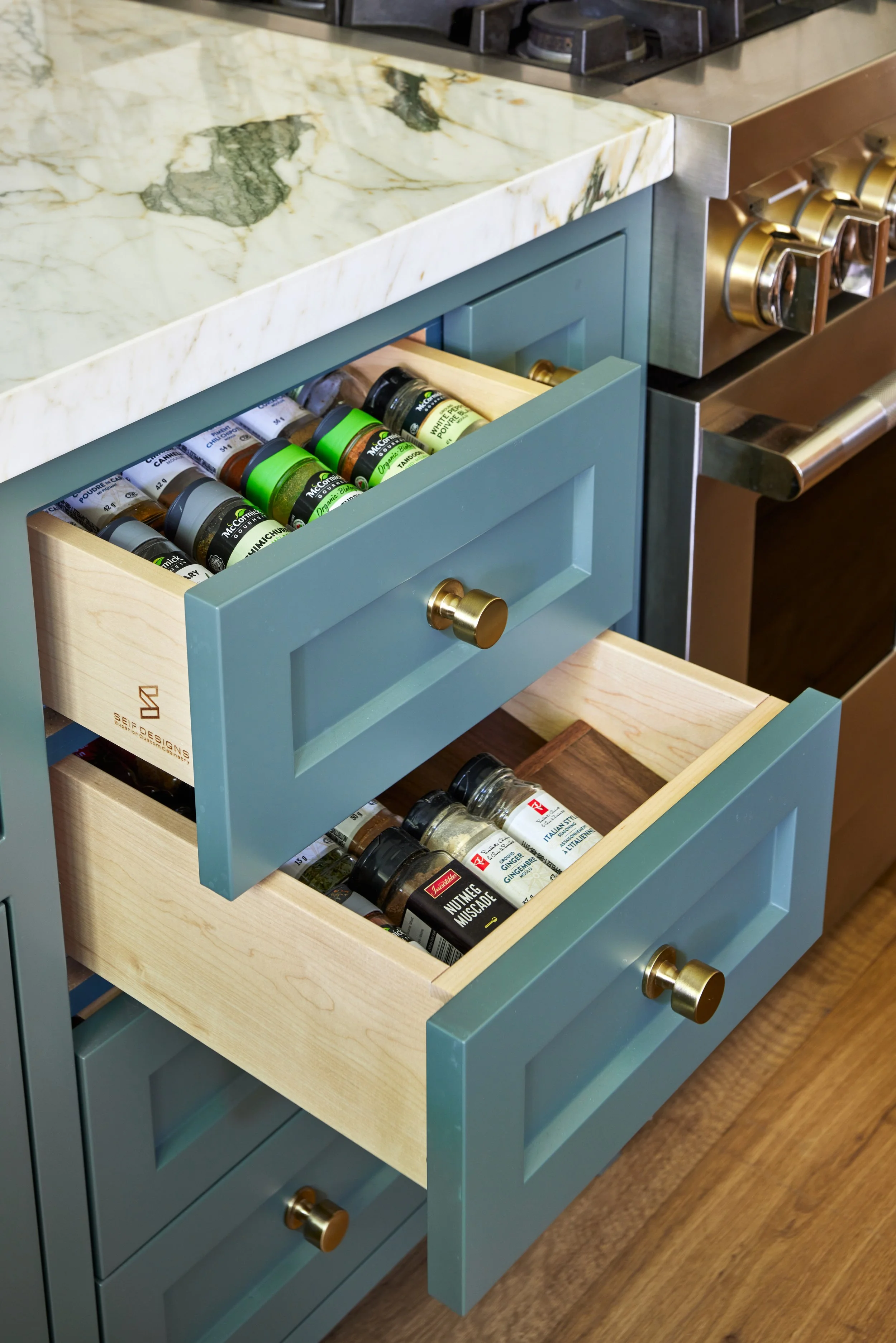 High-end custom modern kitchen in Mississauga, Oakville, and Toronto, Ontario. Features trends color for 2024, luxurious gold hardware, a marble countertop, an elegant kitchen sink, custom shelving with a pocket door, and efficient kitchen and drawer