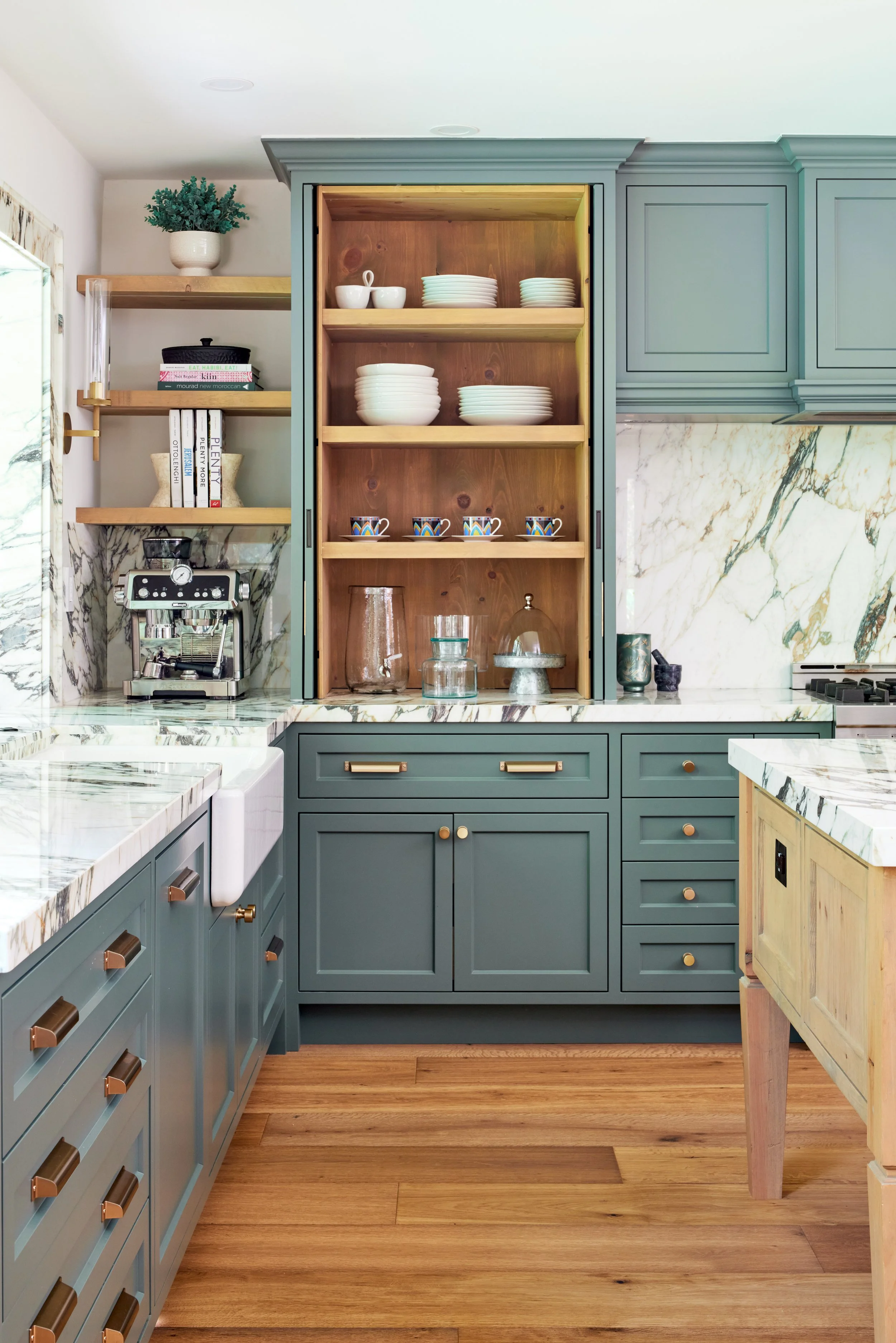 High-end custom modern kitchen in Mississauga, Oakville, and Toronto, Ontario. Features trends color for 2024, luxurious gold hardware, a marble countertop, an elegant kitchen sink, and custom shelving with a pocket door. Serving millwork and cabinet