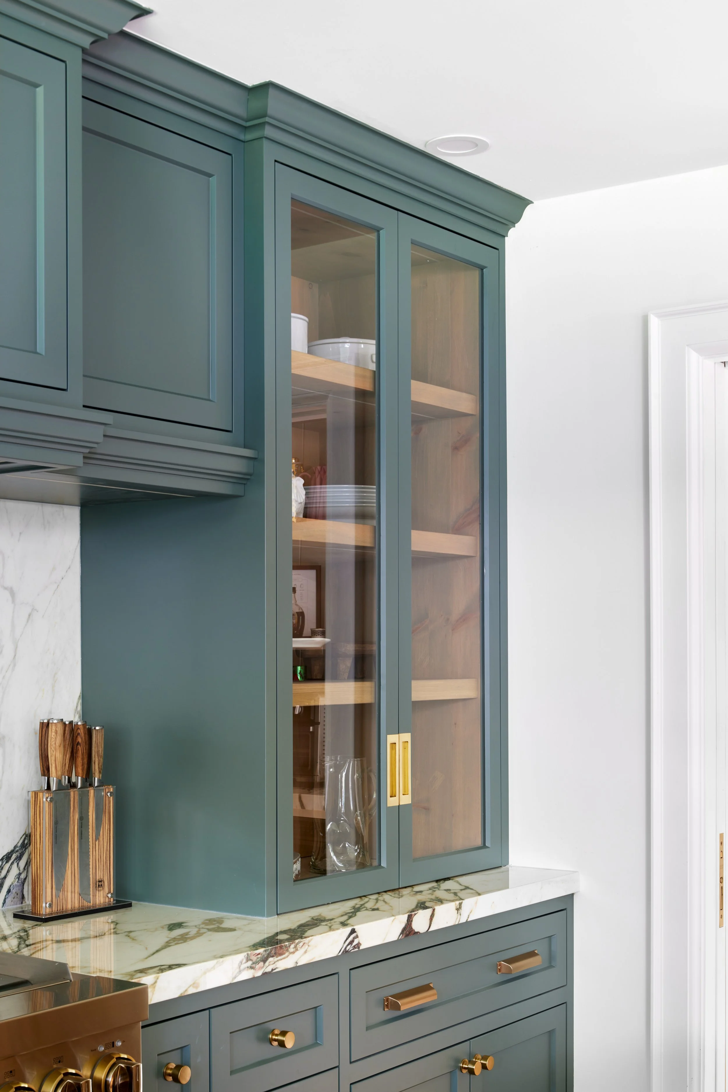 High-end custom modern kitchen in Mississauga, Oakville, and Toronto, Ontario. Features trends color for 2024, luxurious gold hardware, a marble countertop, an elegant kitchen sink, and custom shelving with a pocket door. Serving millwork and cabinet