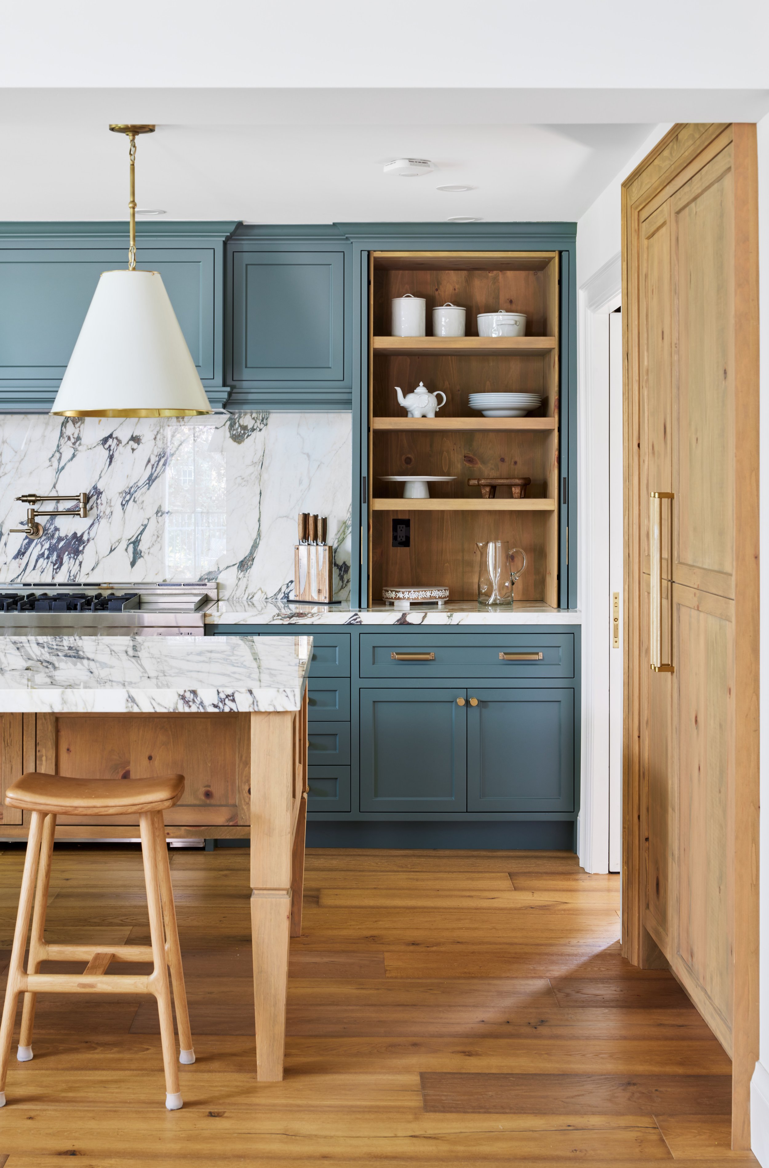High-end custom modern kitchen in Mississauga, Oakville, and Toronto, Ontario. Features trends color for 2024, luxurious gold hardware, a marble countertop, an elegant kitchen sink, custom shelving with a pocket door, and efficient kitchen and drawer
