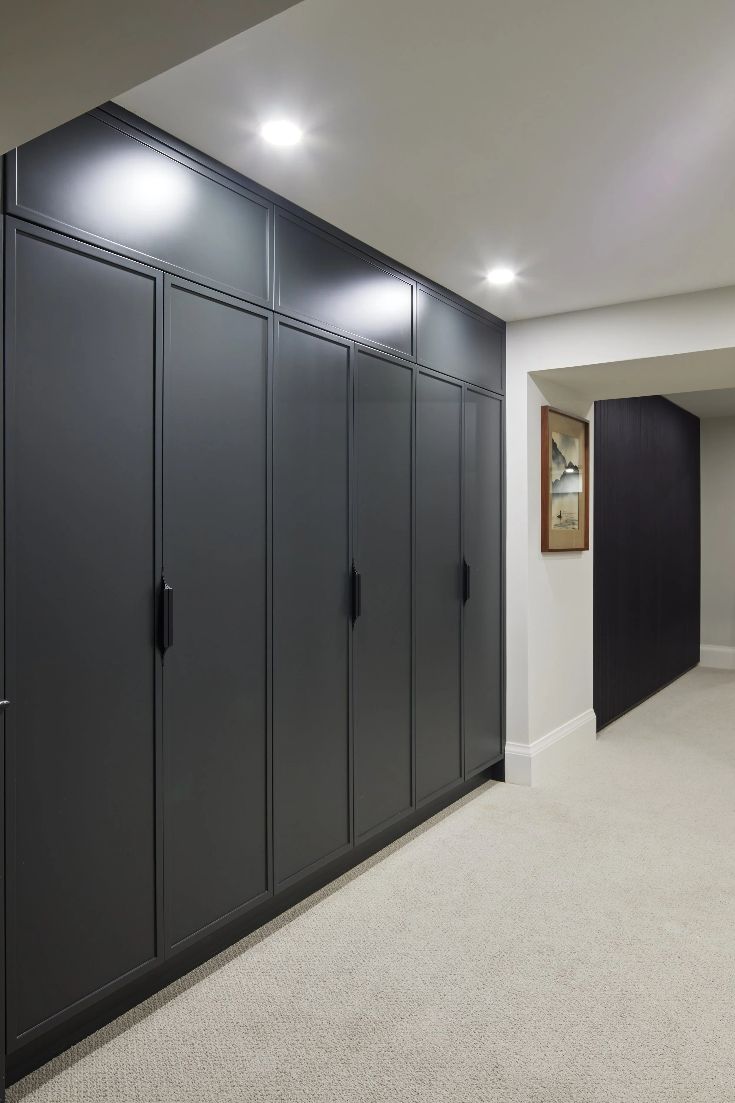 Custom closet cabinetry in matte black with minimalist handles, cabinet from floor to ceiling to maximize storage with smooth, clean lines design, custom closet with hidden door near me across Greater Toronto Area, Mississauga, Oakville.