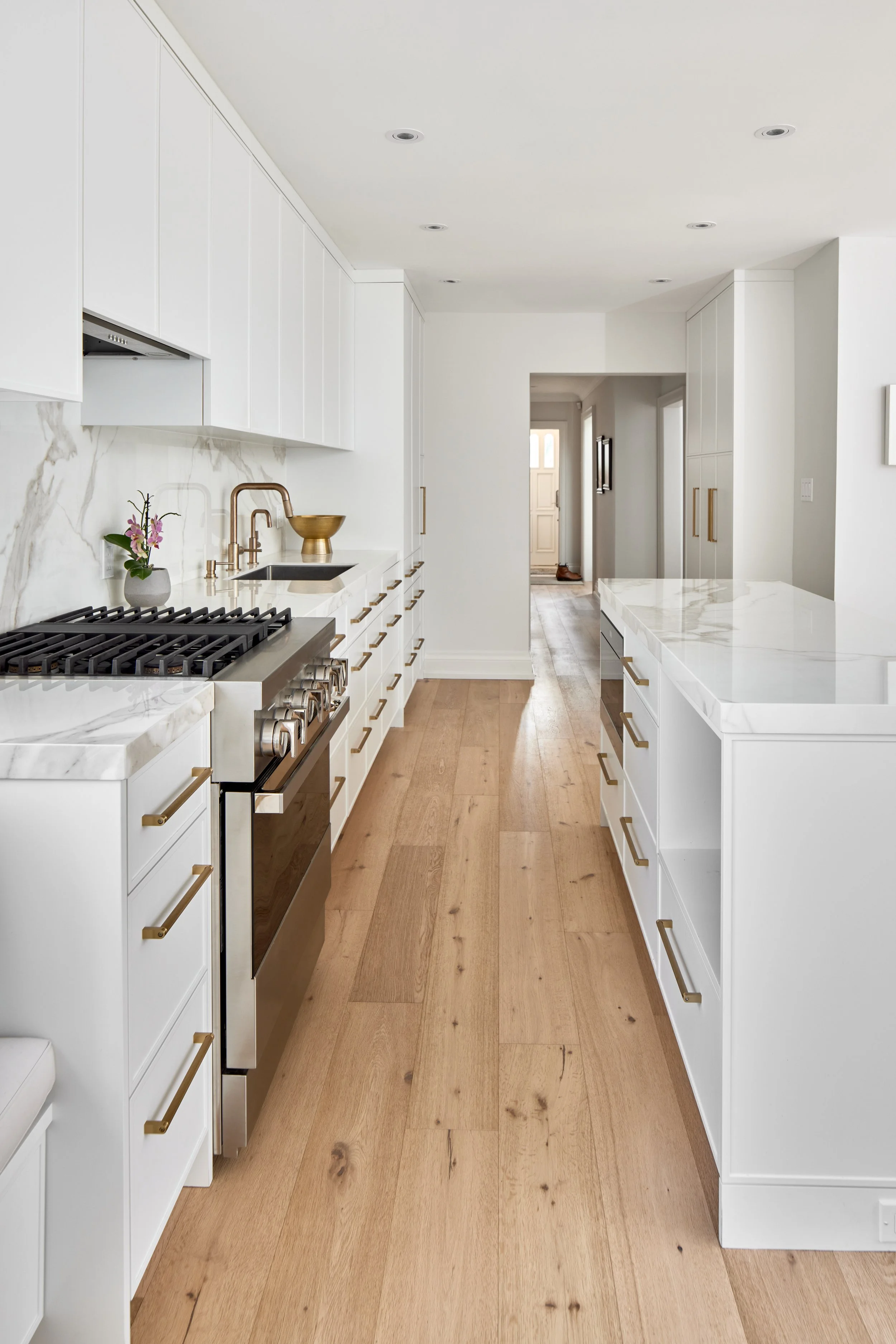 Modern custom kitchen features high-end brass fixtures and an undermount sink. High-end custom modern kitchen in Mississauga, Oakville, and Toronto, Ontario. Features trends color for 2024, luxurious gold hardware, a marble countertop, an elegant kit