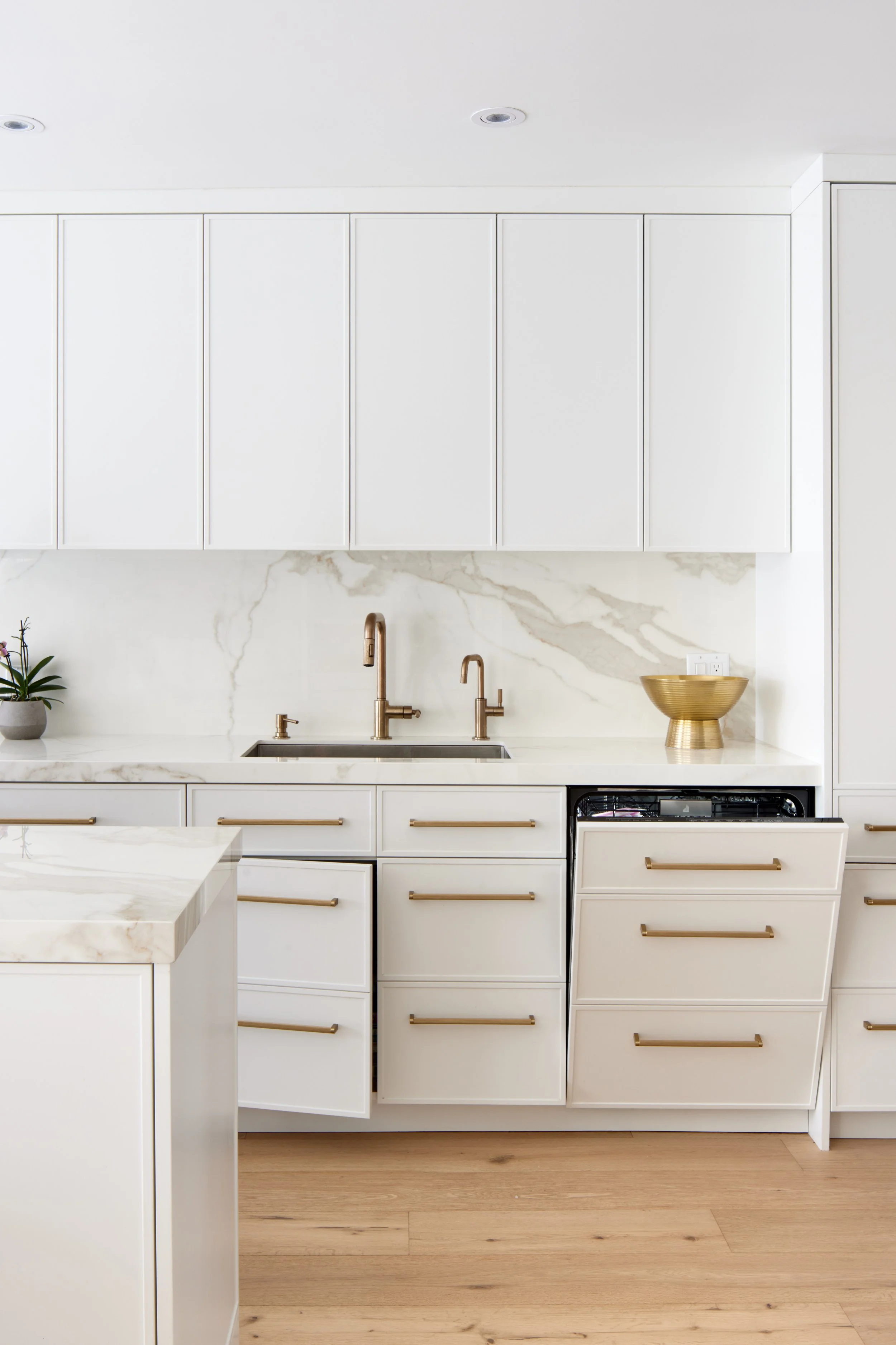 Modern custom kitchen features high-end brass fixtures and an undermount sink. High-end custom modern kitchen in Mississauga, Oakville, and Toronto, Ontario. Features trends color for 2024, luxurious gold hardware, a marble countertop, an elegant kit