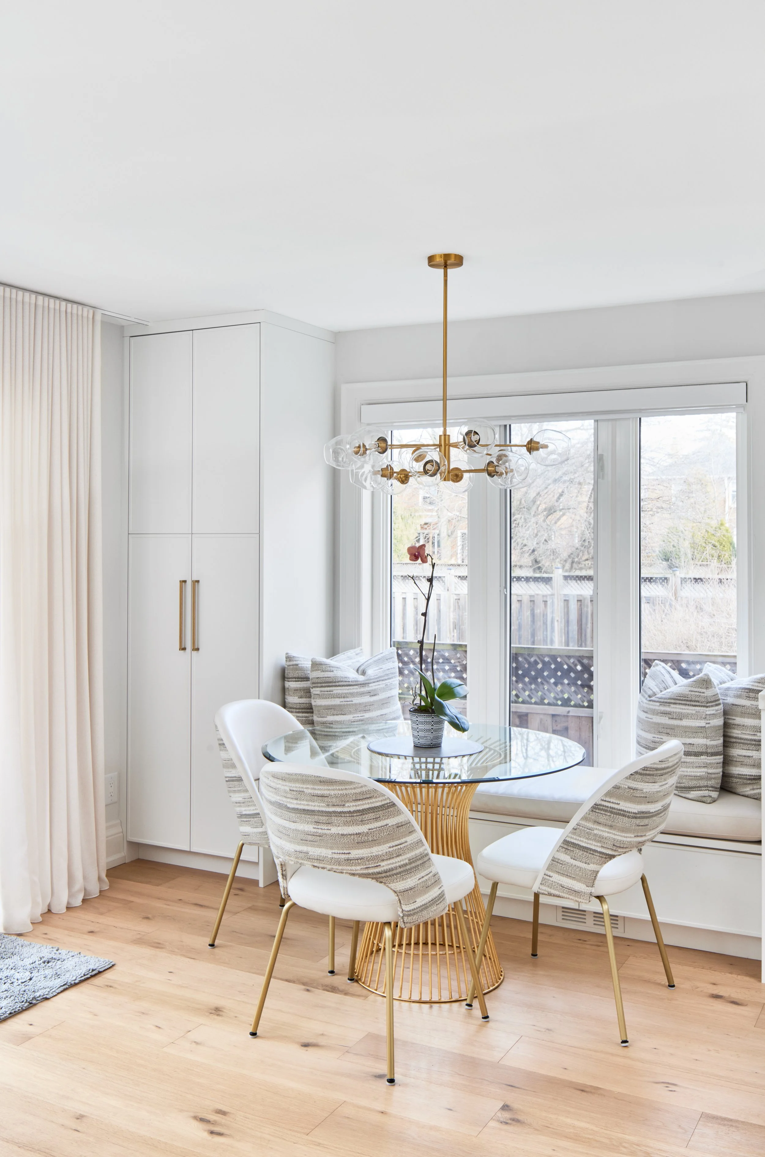 Explore This Beautiful Kitchen: See a modern kitchen with clean white cabinets and beautiful marble. It's well-designed with gold handles and light wood floors that make the space look bright and welcoming. Nearby, a window bench in the dining area o
