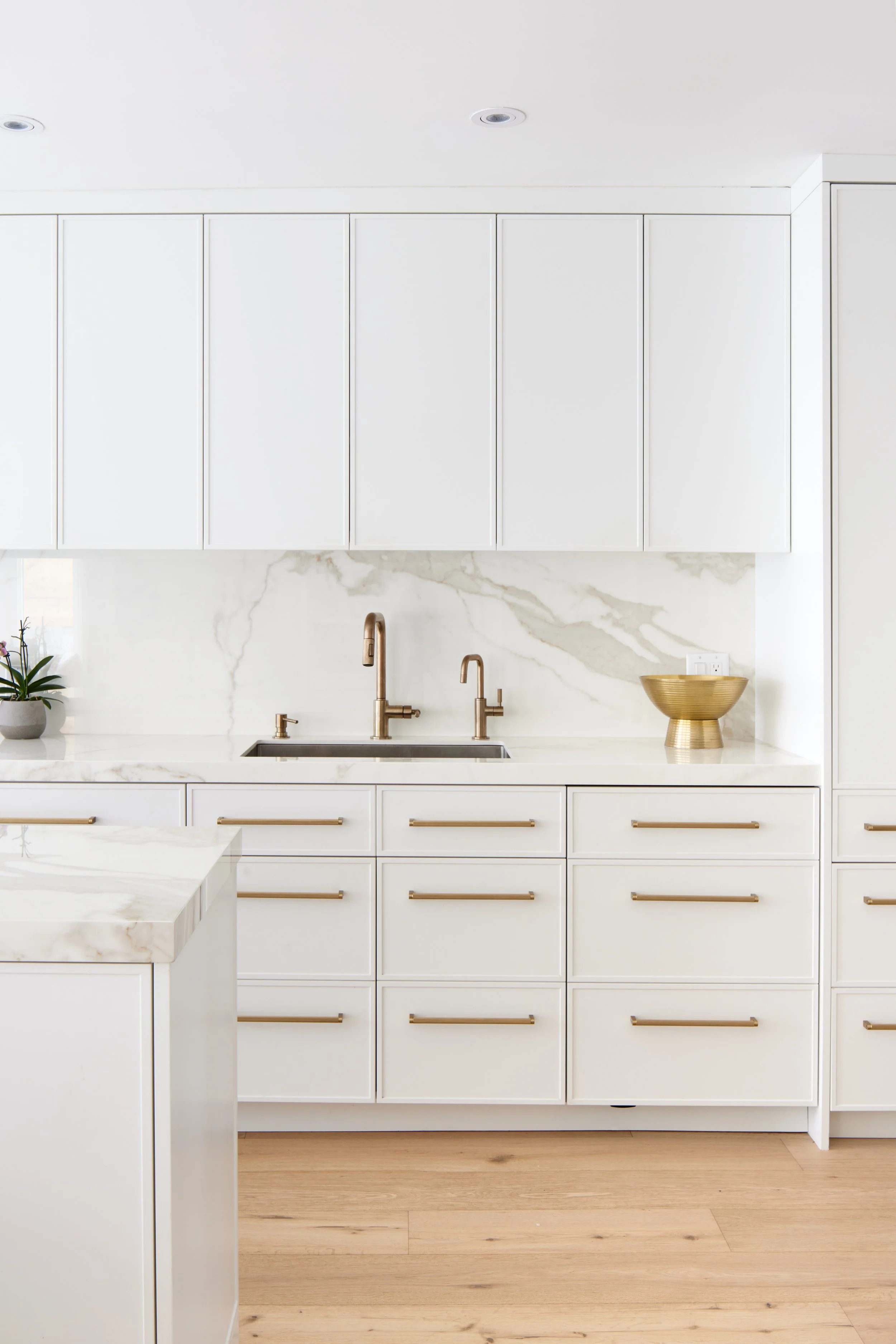 Modern custom kitchen features high-end brass fixtures and an undermount sink. High-end custom modern kitchen in Mississauga, Oakville, and Toronto, Ontario. Features trends color for 2024, luxurious gold hardware, a marble countertop, an elegant kit