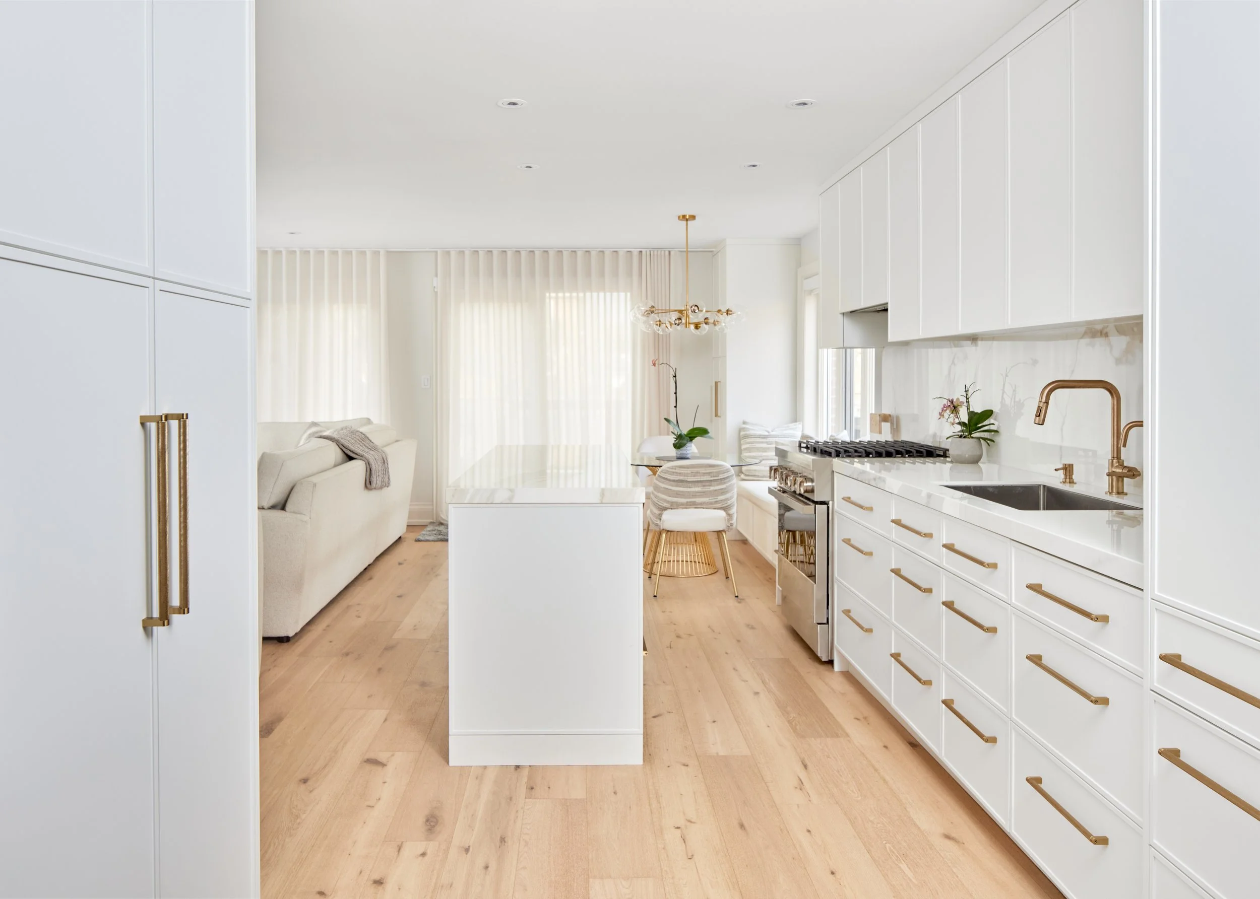 Bright Open Kitchen: This kitchen features beautiful white cabinets and marble details, creating a fresh, inviting space. The design includes a practical island for cooking and dining. Nearby, a window bench in the dining area offers a cozy spot to e