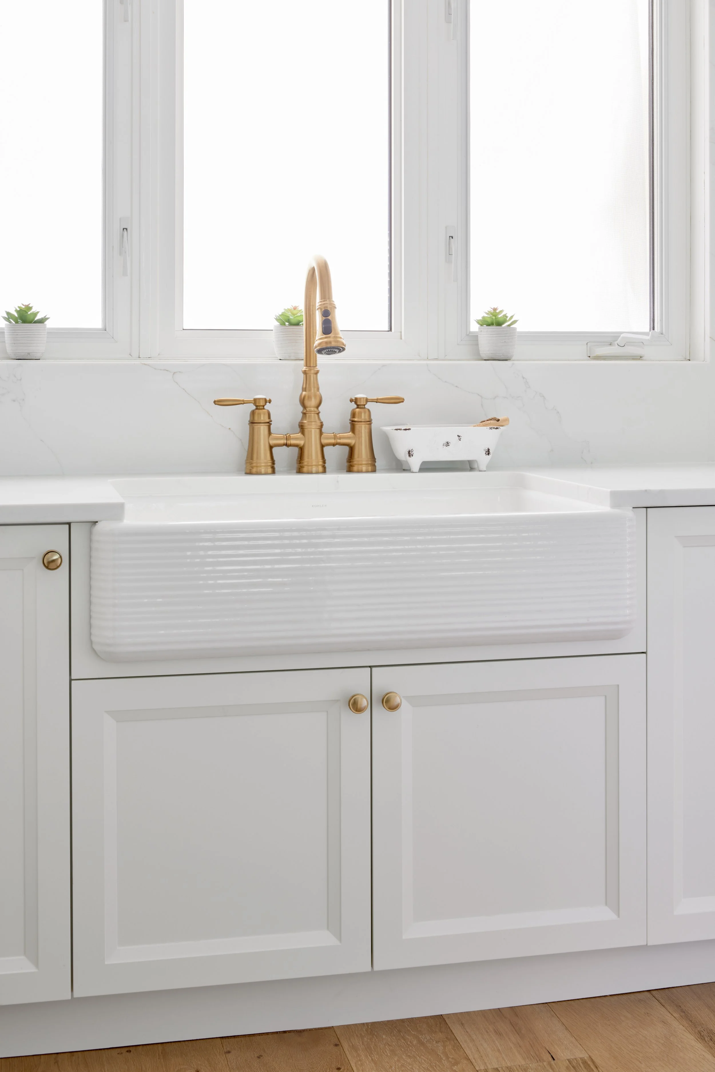 Modern custom kitchen features high-end brass fixtures and an undermount sink. High-end custom modern kitchen in Mississauga, Oakville, and Toronto, Ontario. Features trends color for 2024, luxurious gold hardware, a marble countertop, an elegant kit