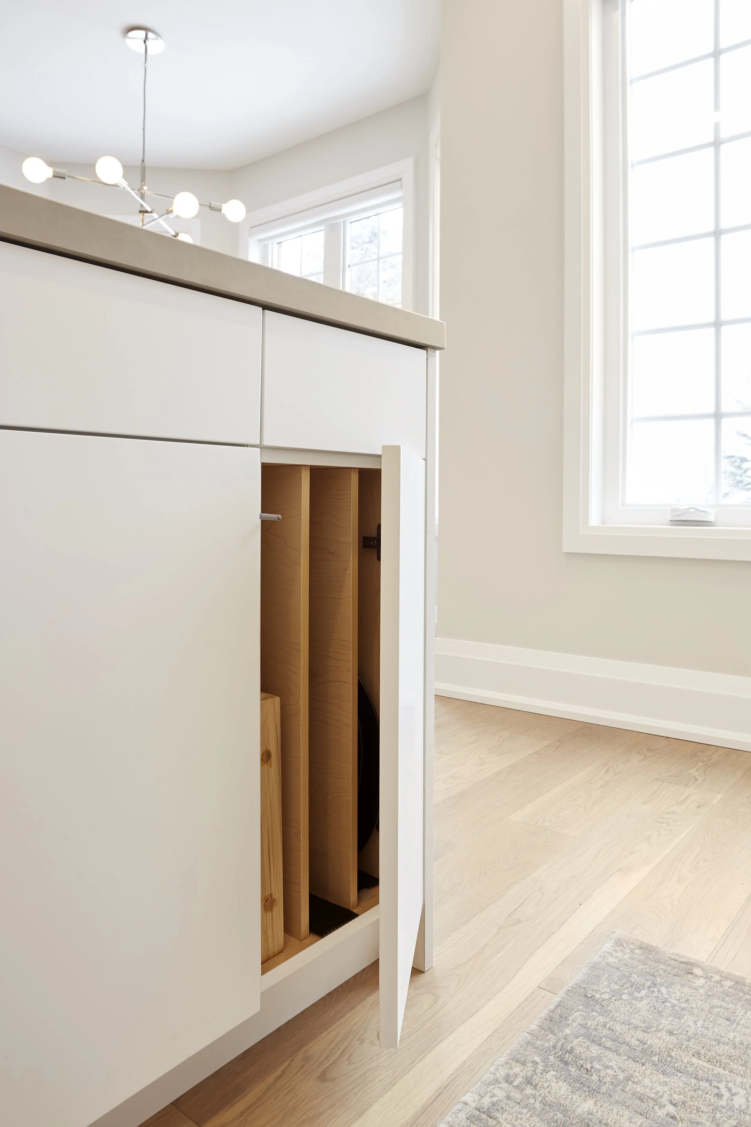 A modern kitchen with white with smart storage solutions. features a tall cabinet with open doors, revealing neatly organized shelves filled with cooking essentials, which makes finding and reaching items easy. A hidden compartment in the island that