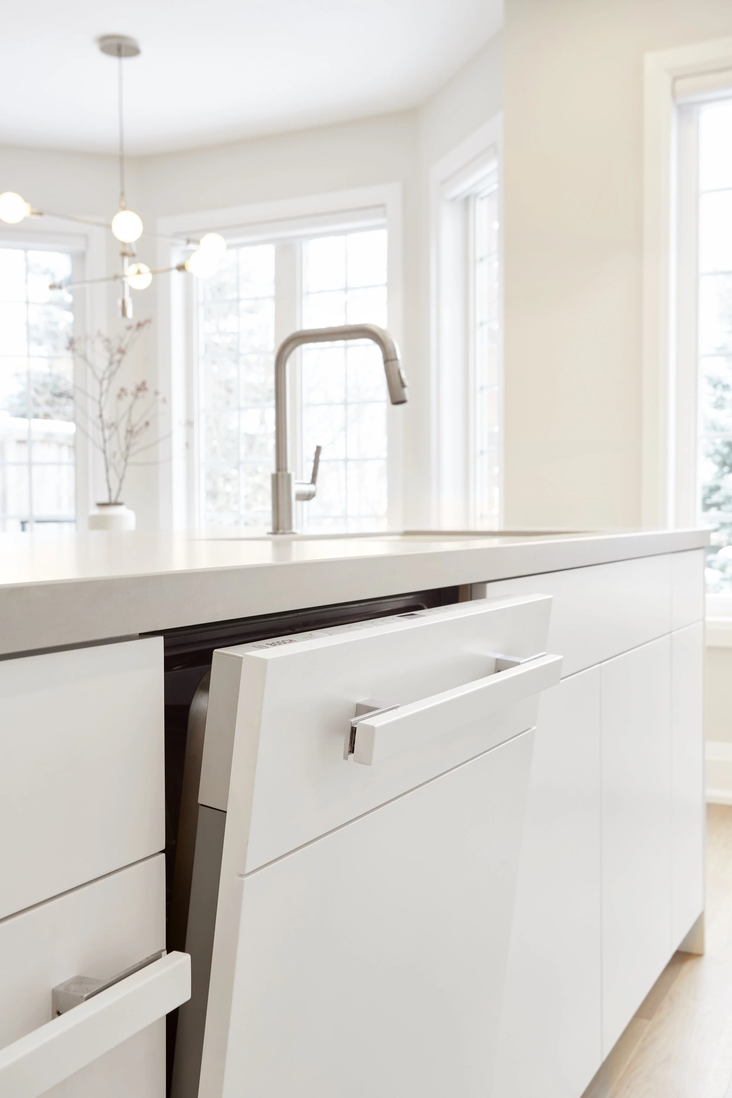 A modern kitchen with white with smart storage solutions. features a tall cabinet with open doors, revealing neatly organized shelves filled with cooking essentials, which makes finding and reaching items easy. A hidden compartment in the island that