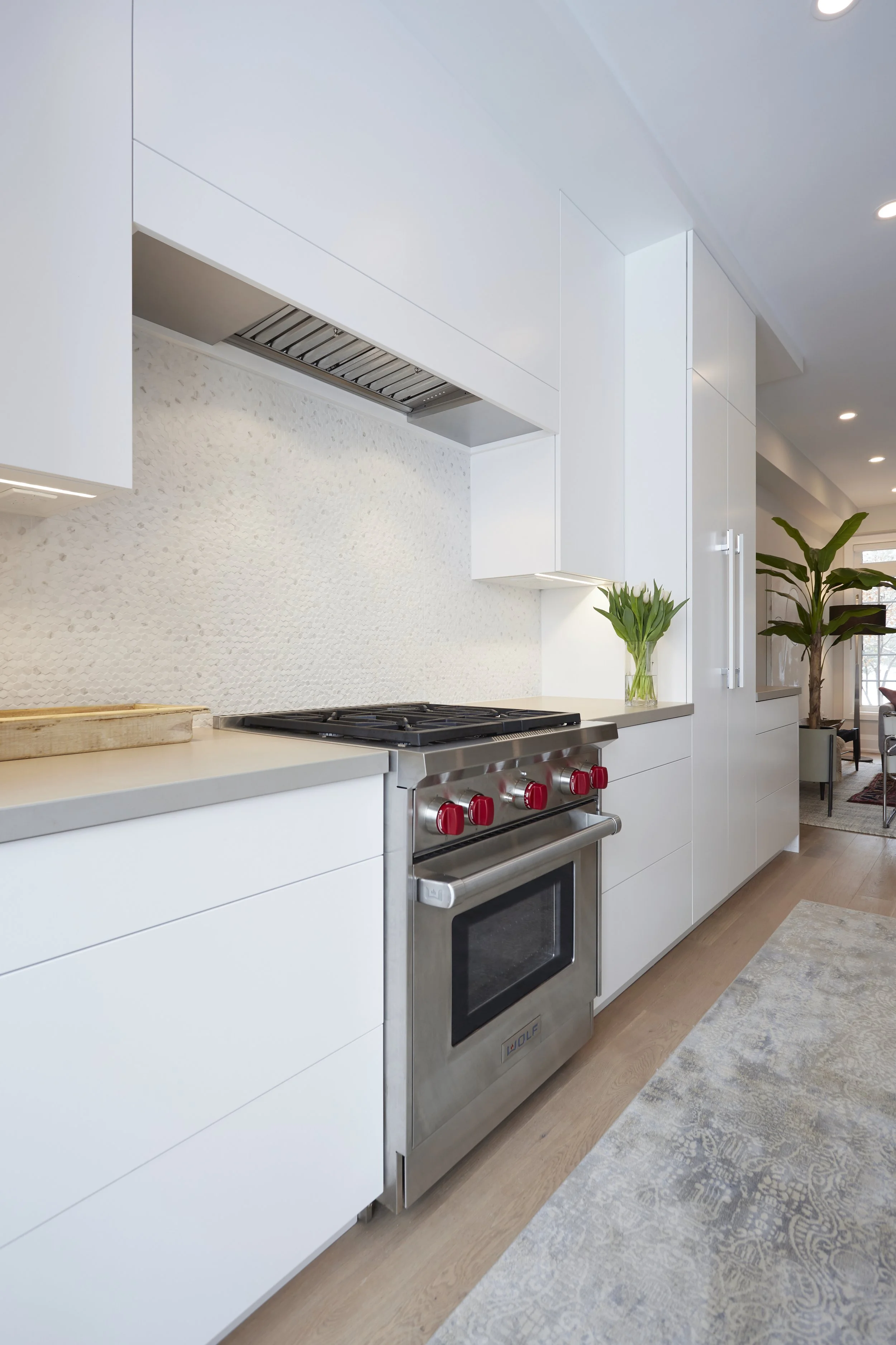 A modern kitchen with white with smart storage solutions. features a tall cabinet with open doors, revealing neatly organized shelves filled with cooking essentials, which makes finding and reaching items easy. A hidden compartment in the island that