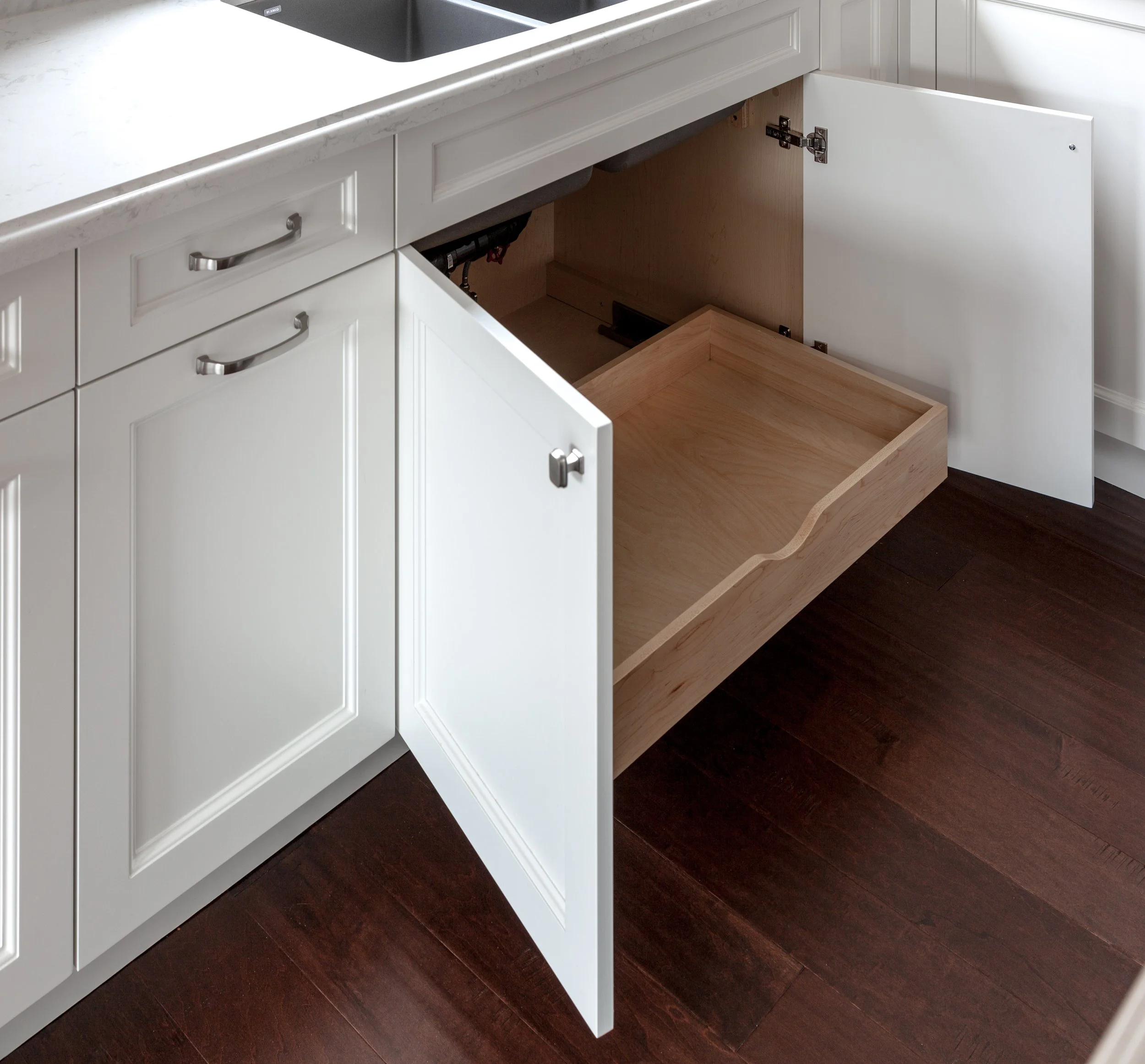 White kitchen cabinet with open drawers showing wooden interior and dark hardwood flooring.