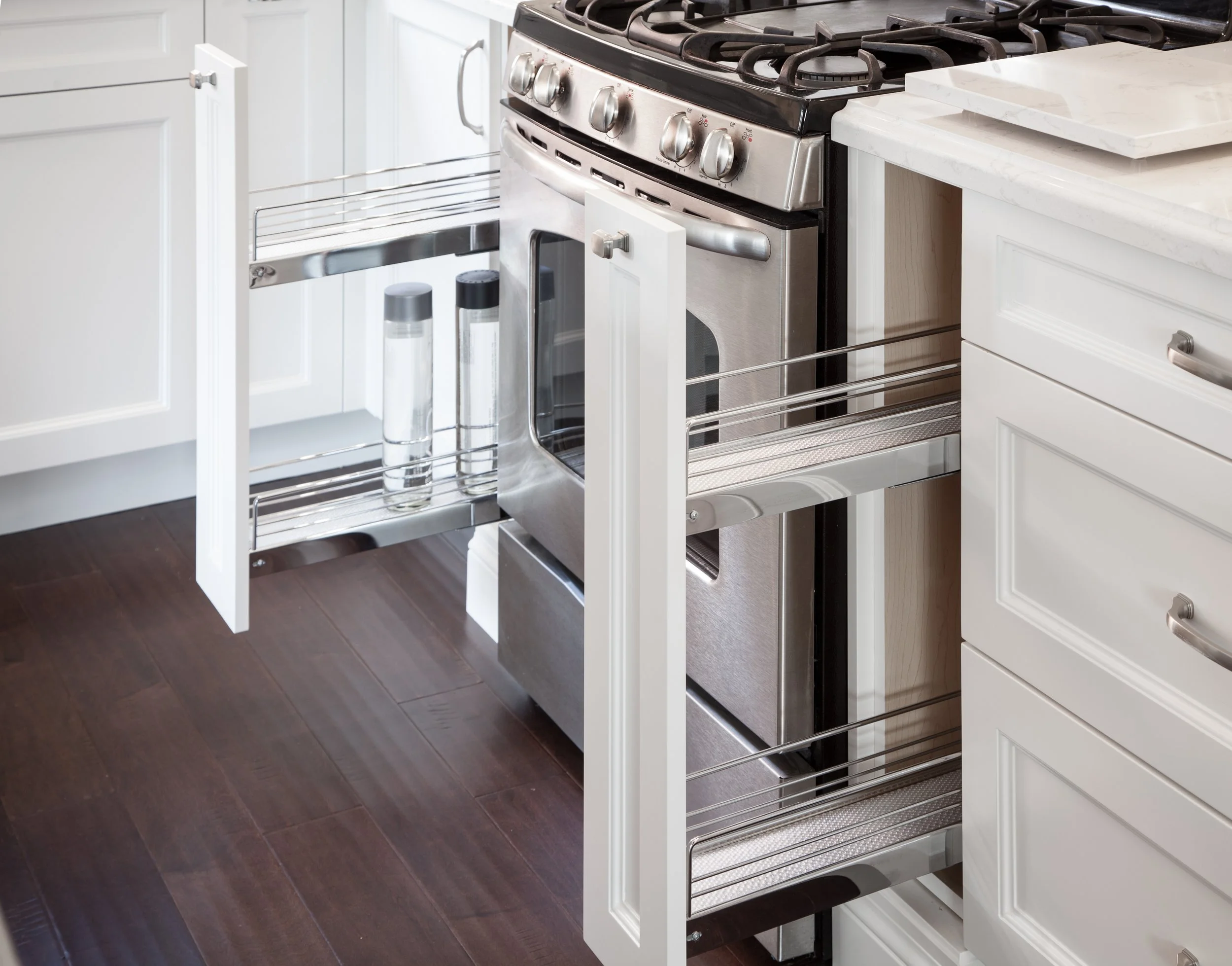 Kitchen with white cabinets and a stainless steel gas oven with an open drawer. Two salt and pepper shakers are on a metal rack in front of the oven, and a white marble countertop is visible on the right.