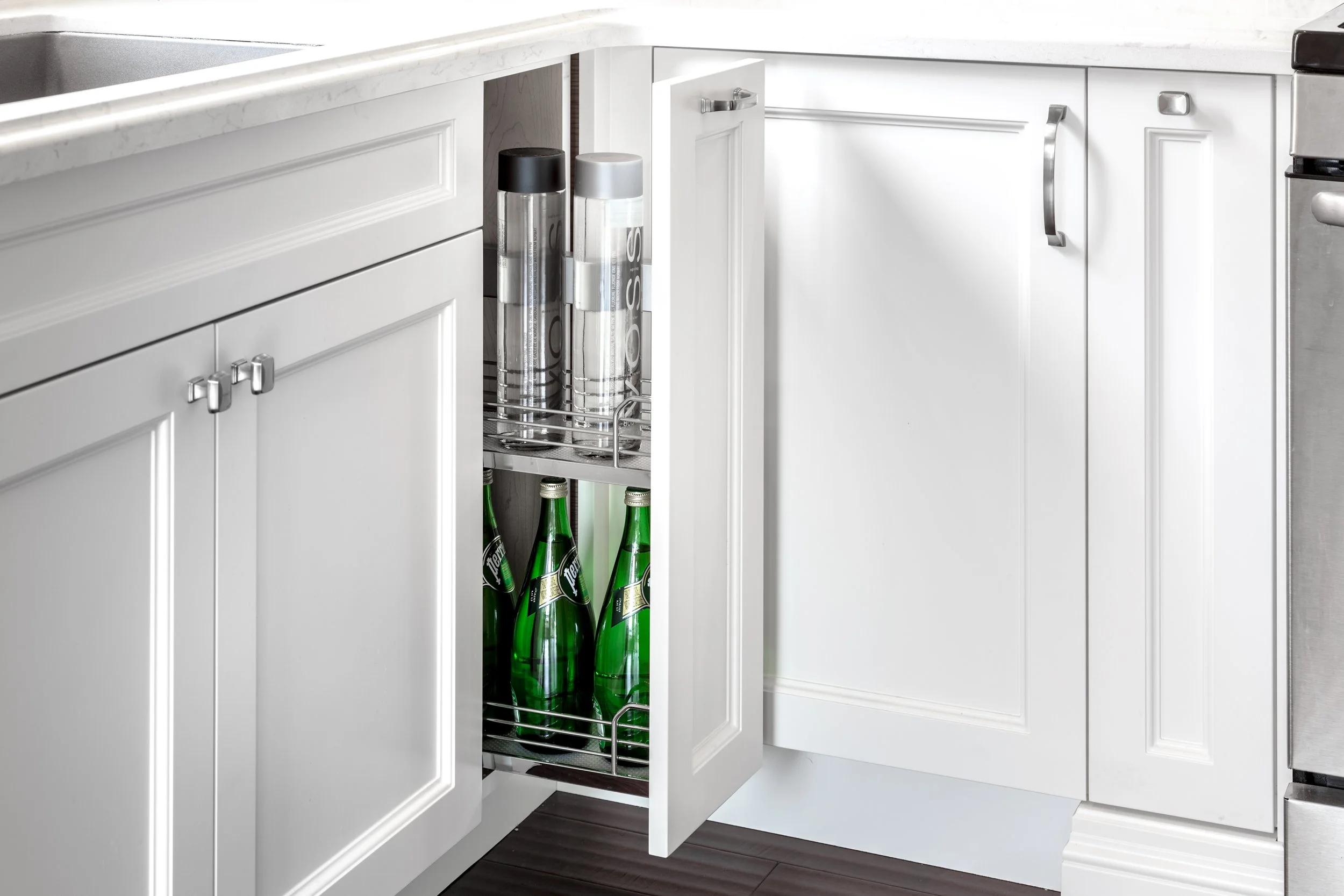 Open kitchen cabinet revealing shelves with green glass bottles, cans, and containers.