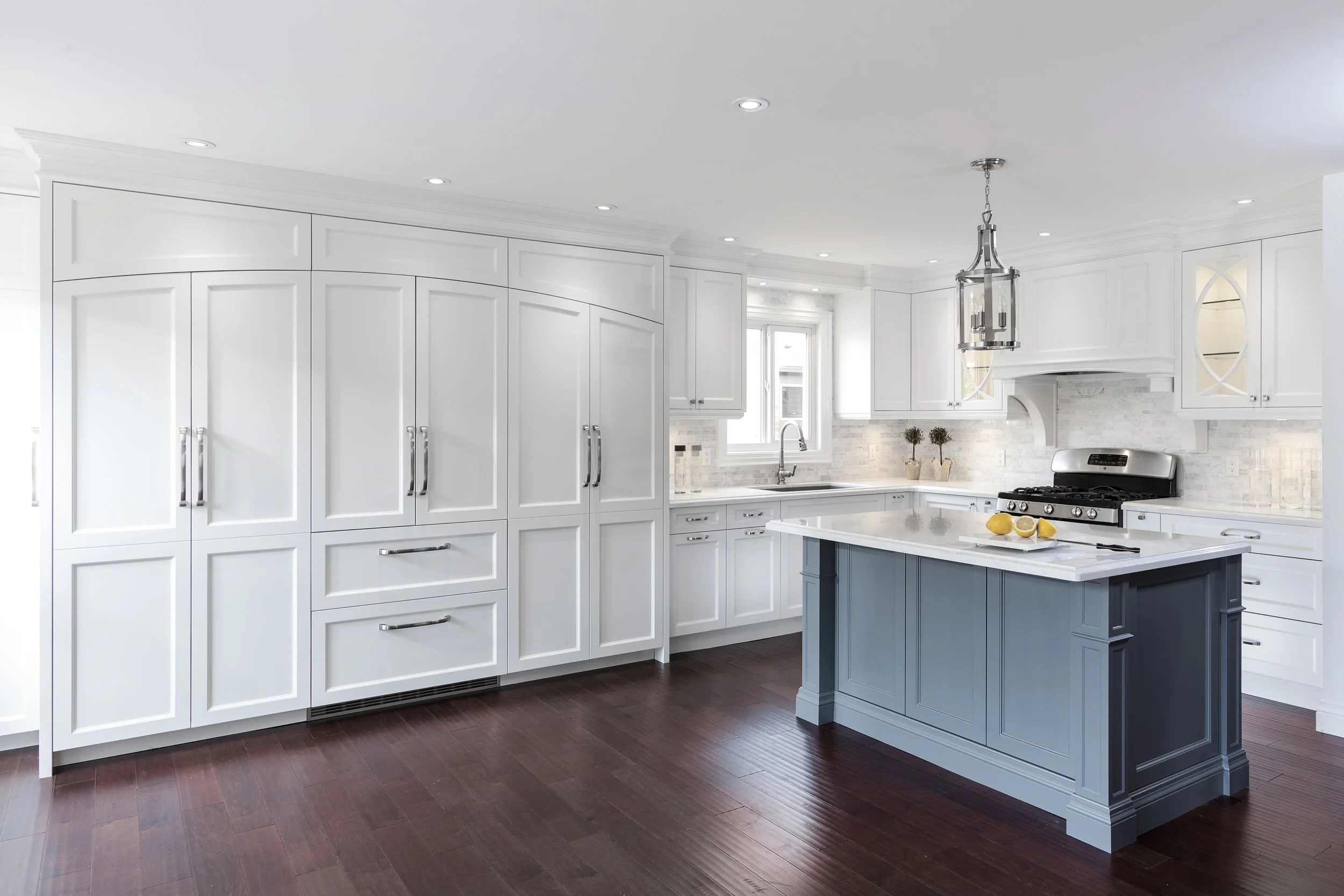 Bright white kitchen with dark wood flooring, white cabinetry, a central island painted blue, and a large chandelier.