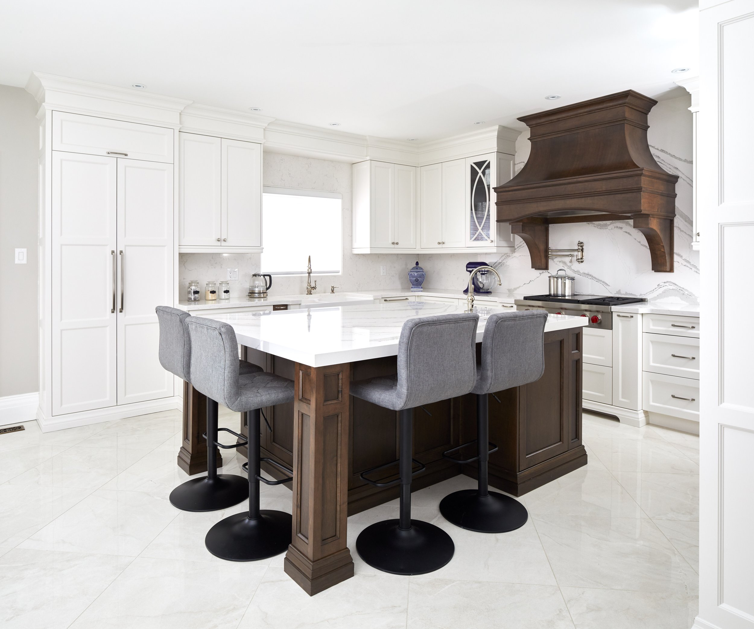 Modern kitchen with white cabinets, marble countertops, a dark wooden island, gray bar stools, and a metal range hood.