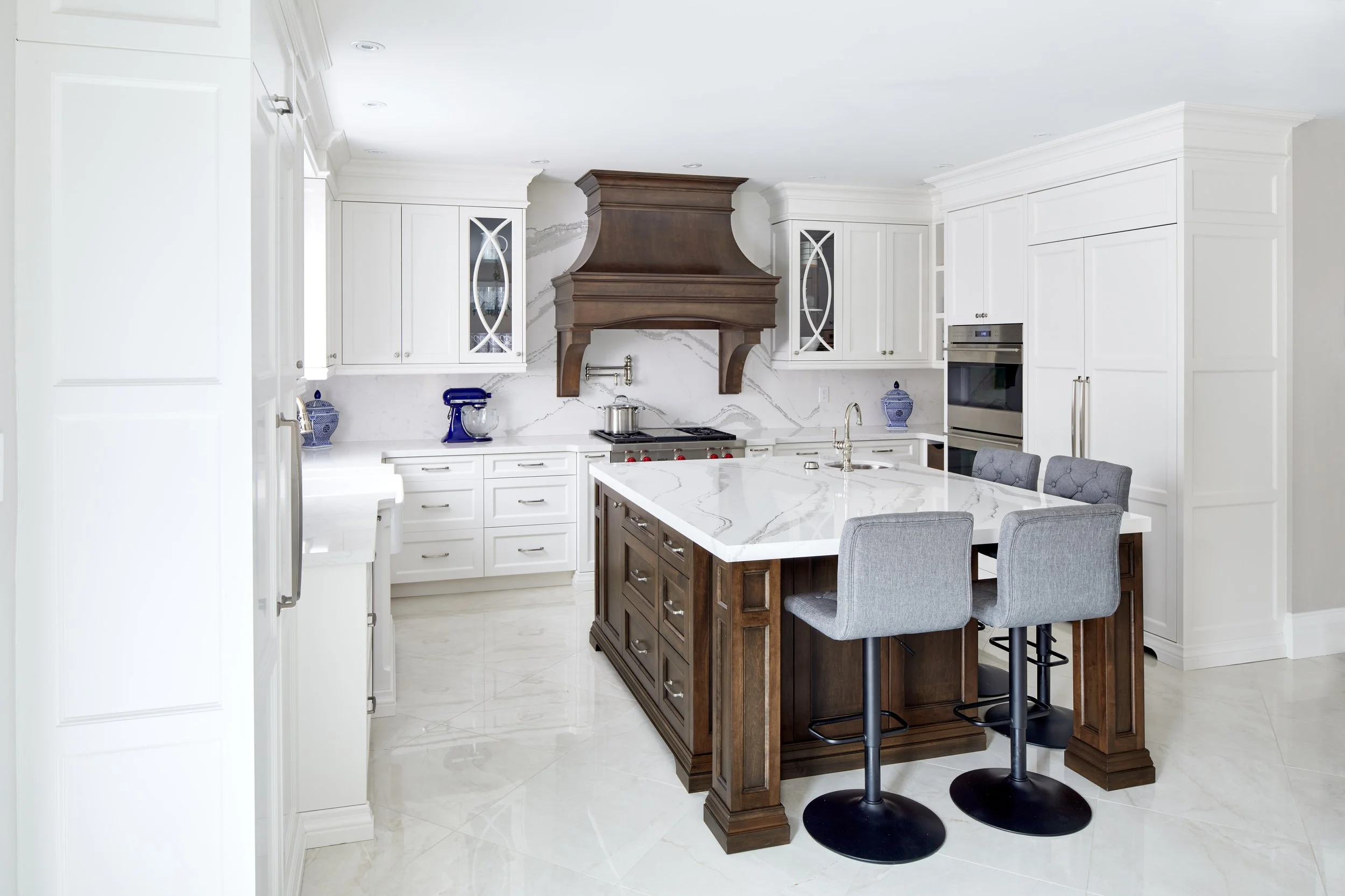 Modern kitchen with white cabinets, marble countertops, a central island with a dark wood base, bar stools, and a stainless steel oven.