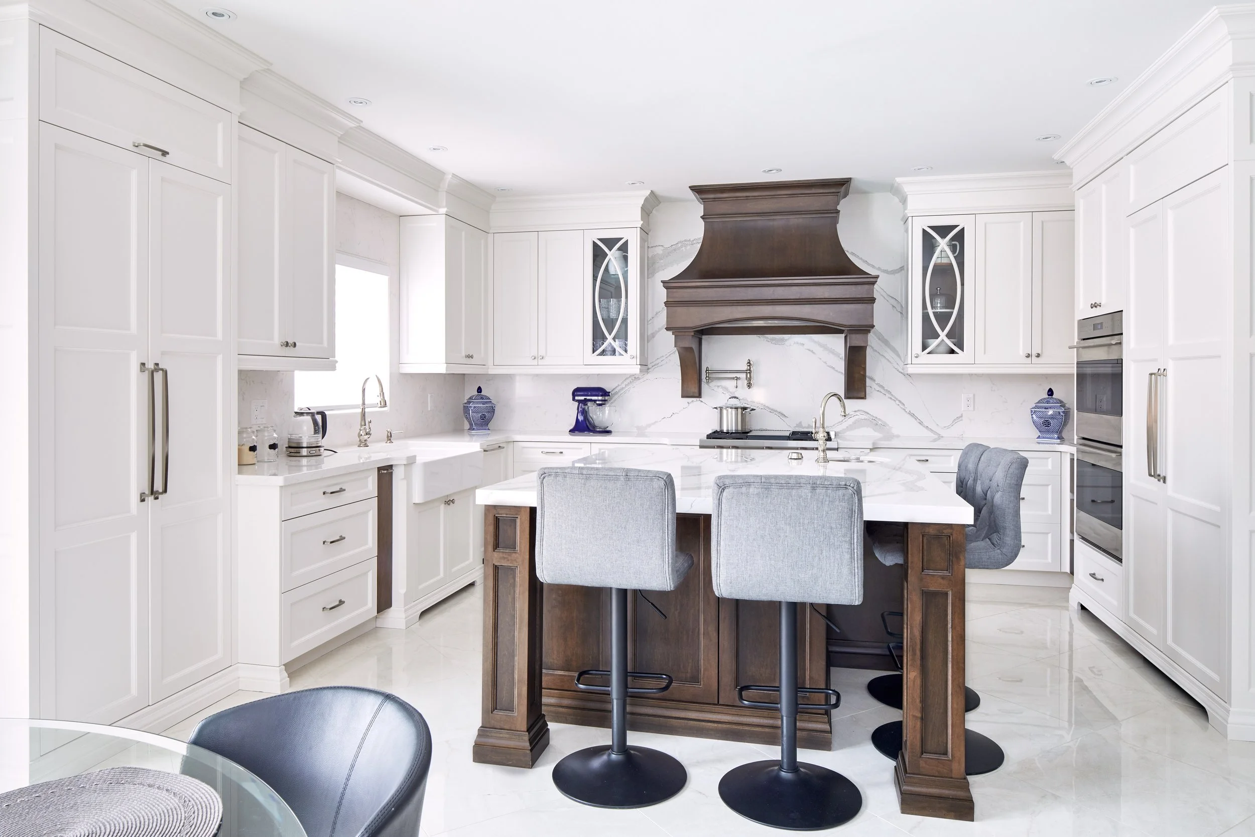 Modern kitchen with white cabinetry, a wooden island with barstools, marble backsplash, and built-in appliances.