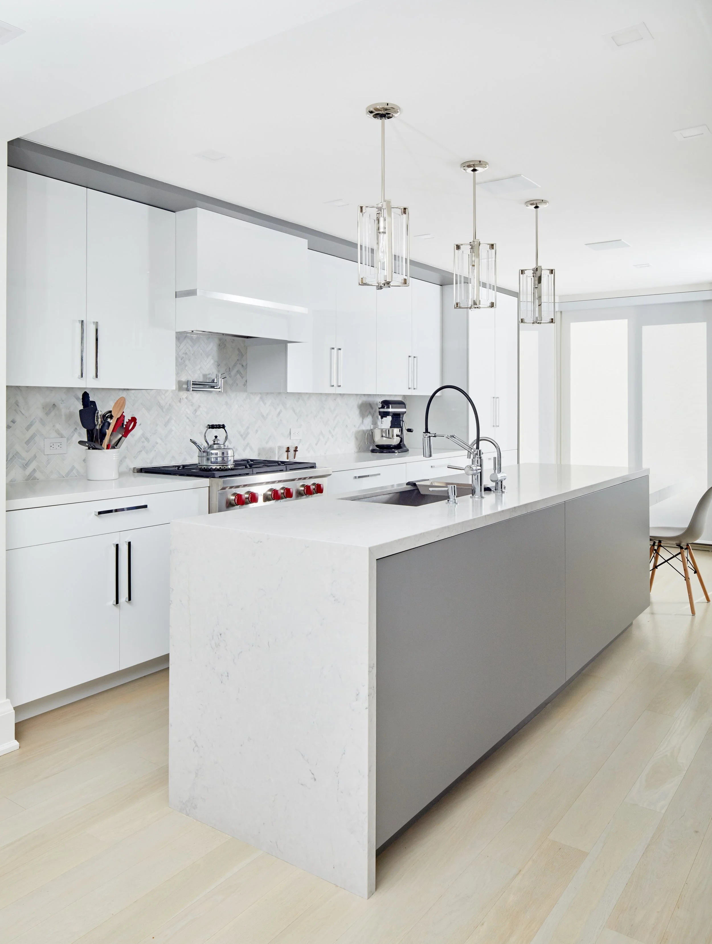 Modern white kitchen with a large island, white cabinetry, pendant lights, and stainless steel appliances.