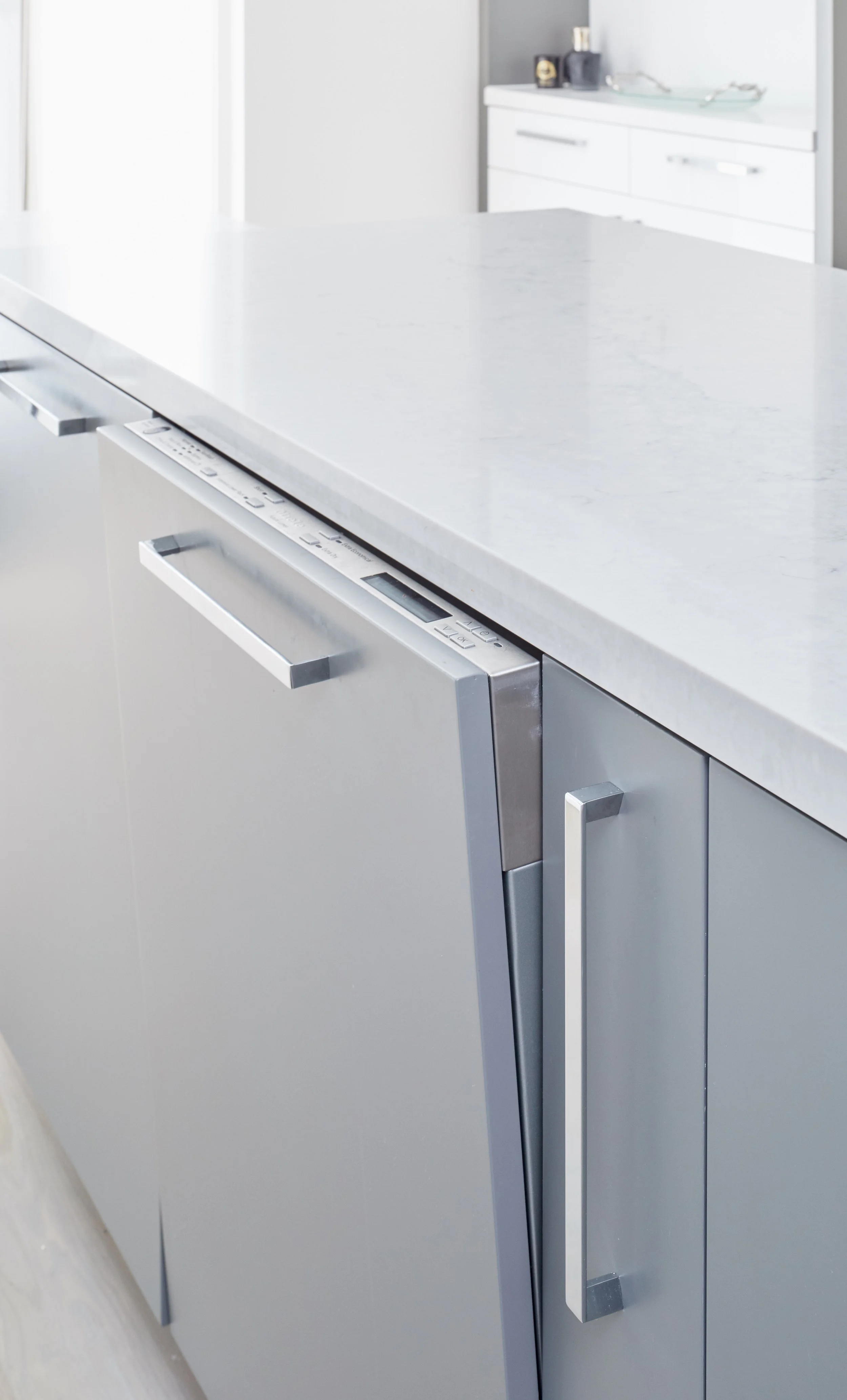 Close-up of a modern white kitchen island with a built-in dishwasher and sleek silver handles.
