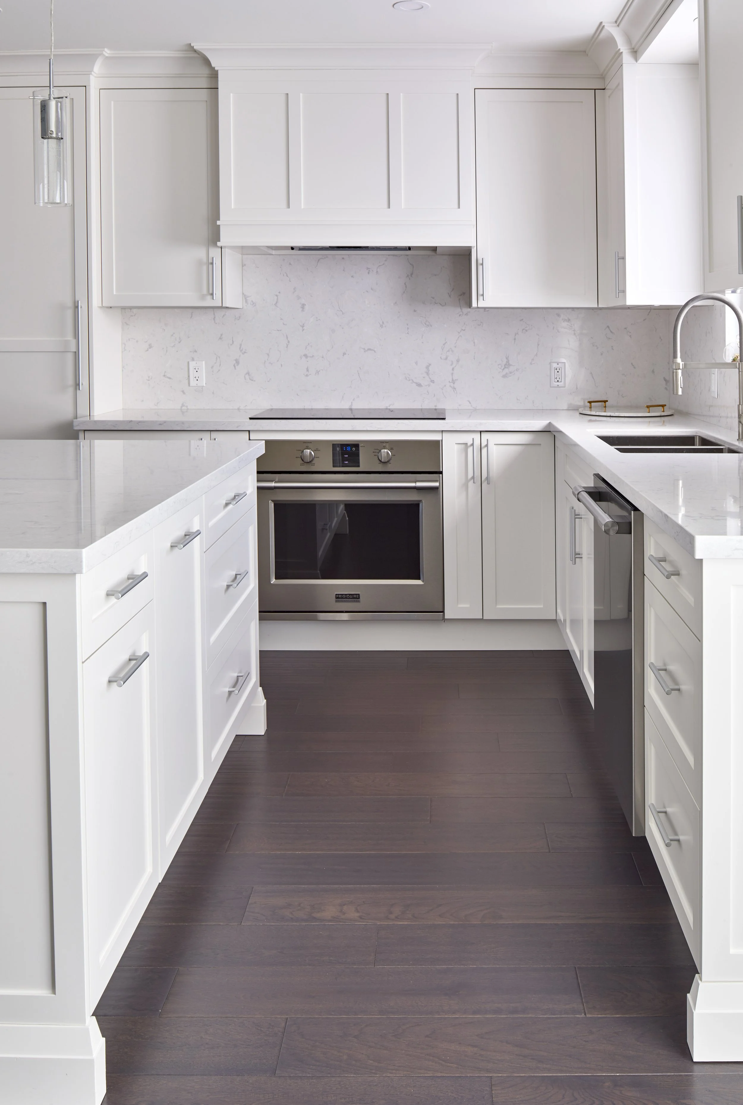 Modern kitchen with white cabinets, marble backsplash, stainless steel oven, and dark wood flooring.