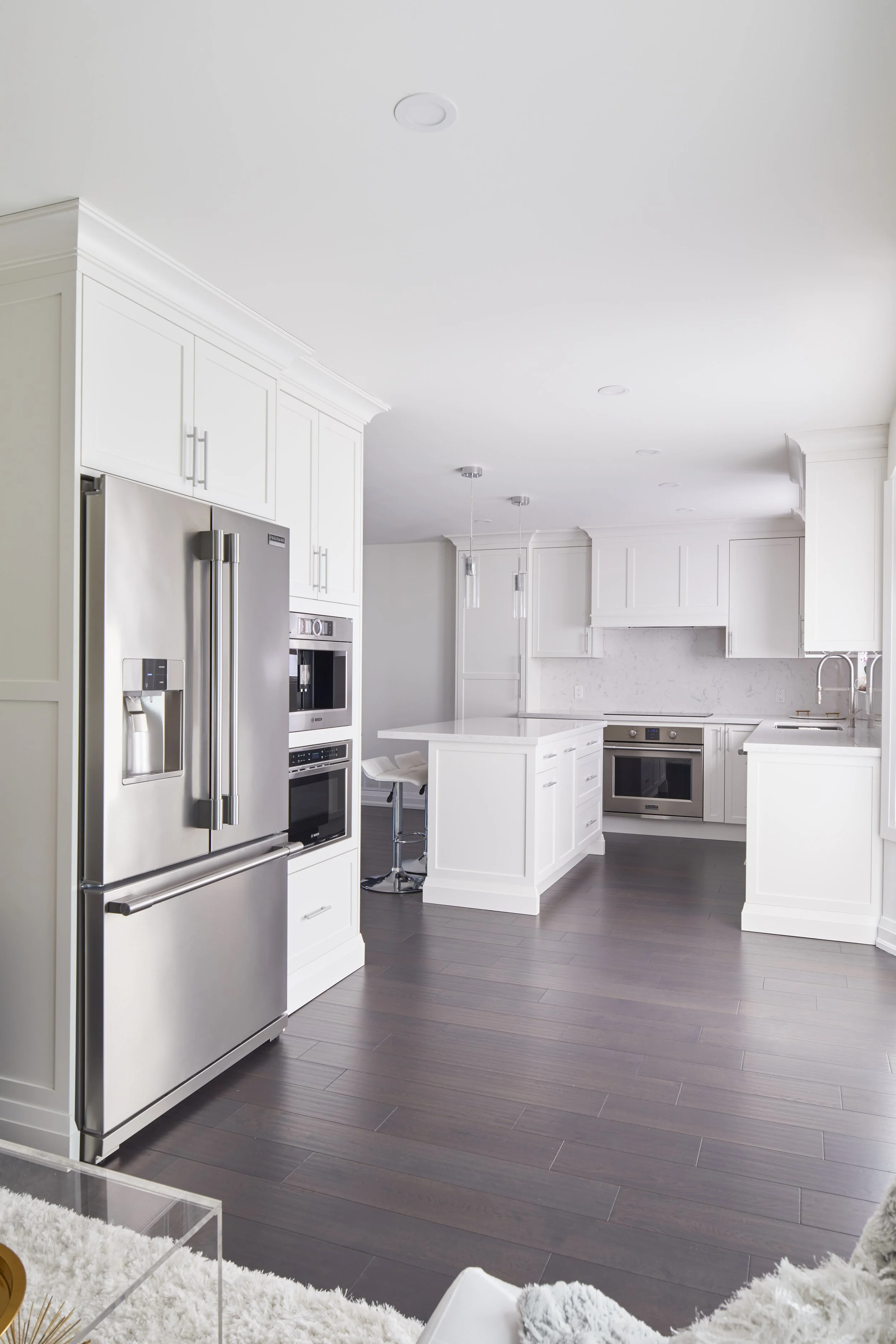 Modern white kitchen with stainless steel appliances, dark wood floors, and pendant lighting.