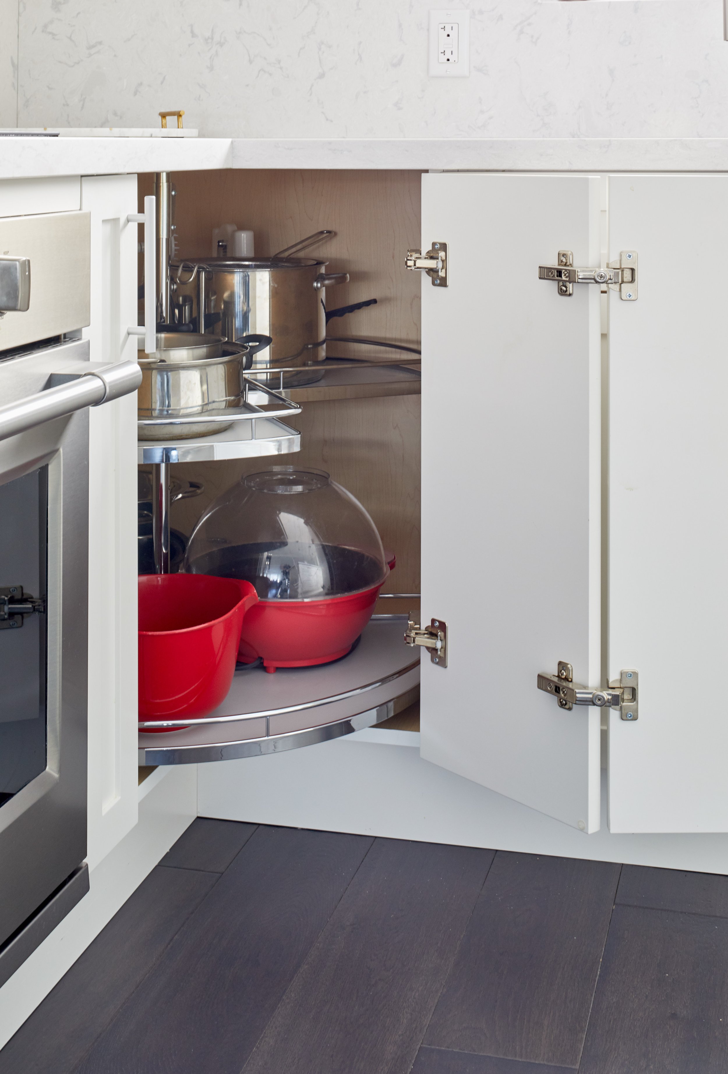 Open white kitchen cabinet with pots, bowls, and kitchen items inside, and purple flooring beneath.