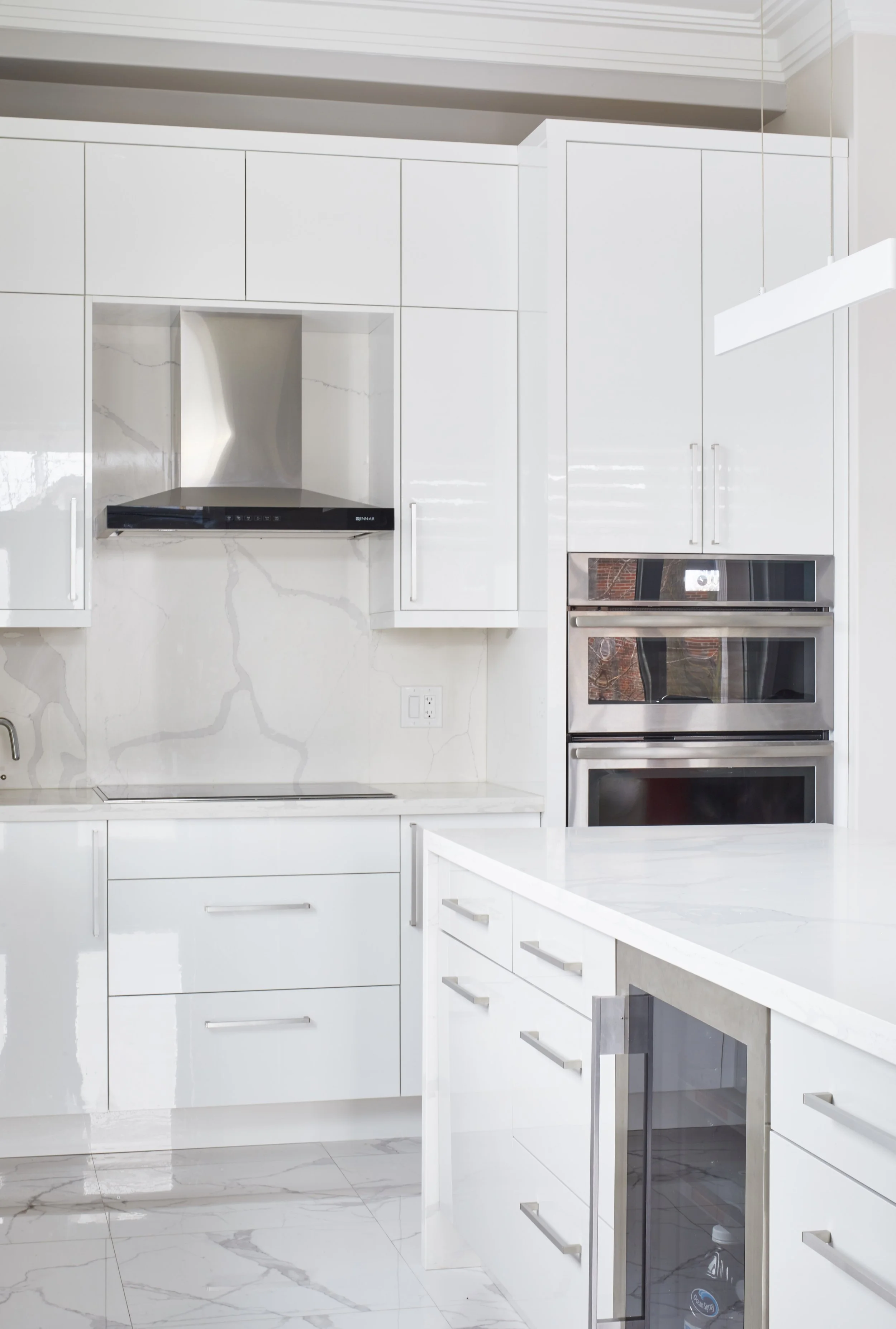 Modern white kitchen with marble flooring, built-in stainless steel appliances, and a white island with a marble top.