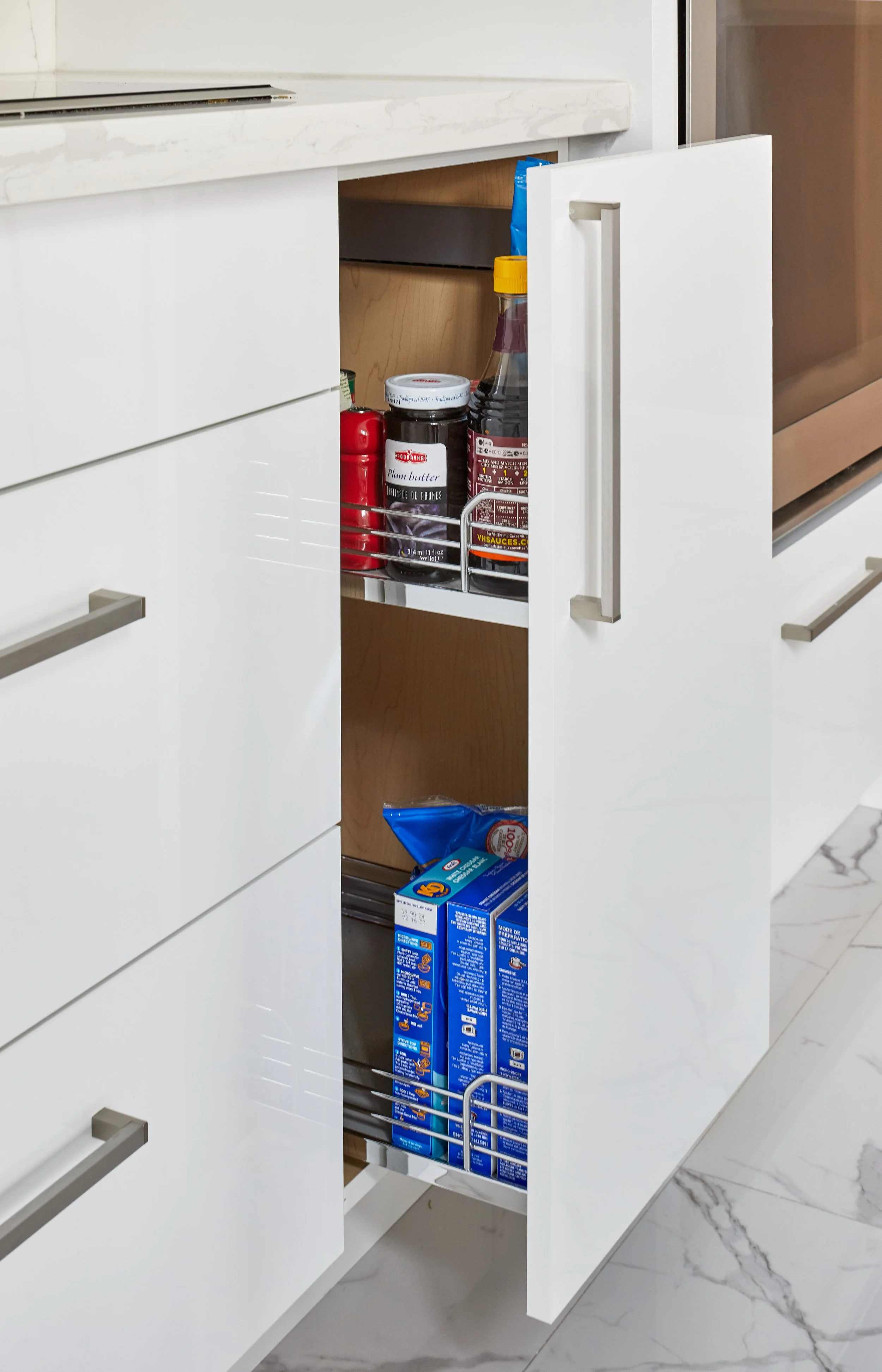 An open kitchen cabinet storing various food items including a jar of plum butter, soy sauce, and other packets.