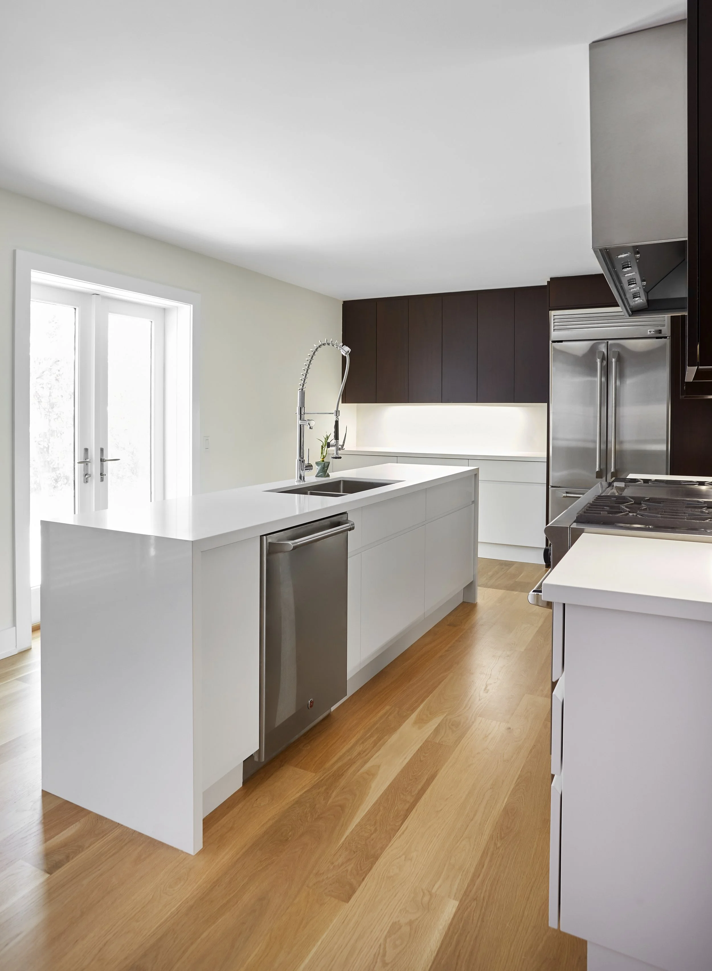 Modern kitchen with white island, stainless steel appliances, dark wood cabinets, and hardwood floors.